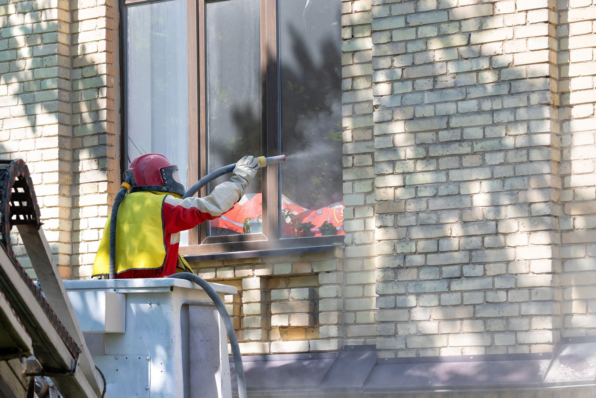 Firefighter spraying water into a burning window of a brick building.