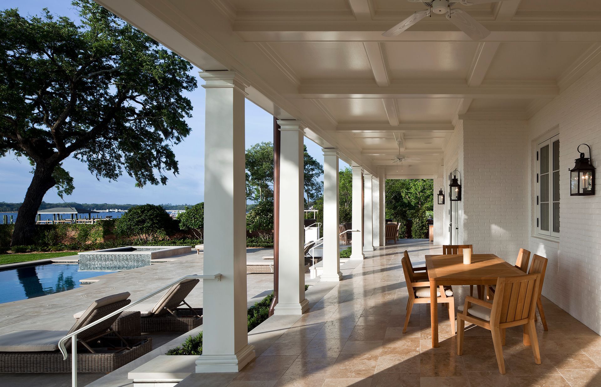 Covered porch with columns, a pool, and wooden furniture, in a bright, outdoor setting.