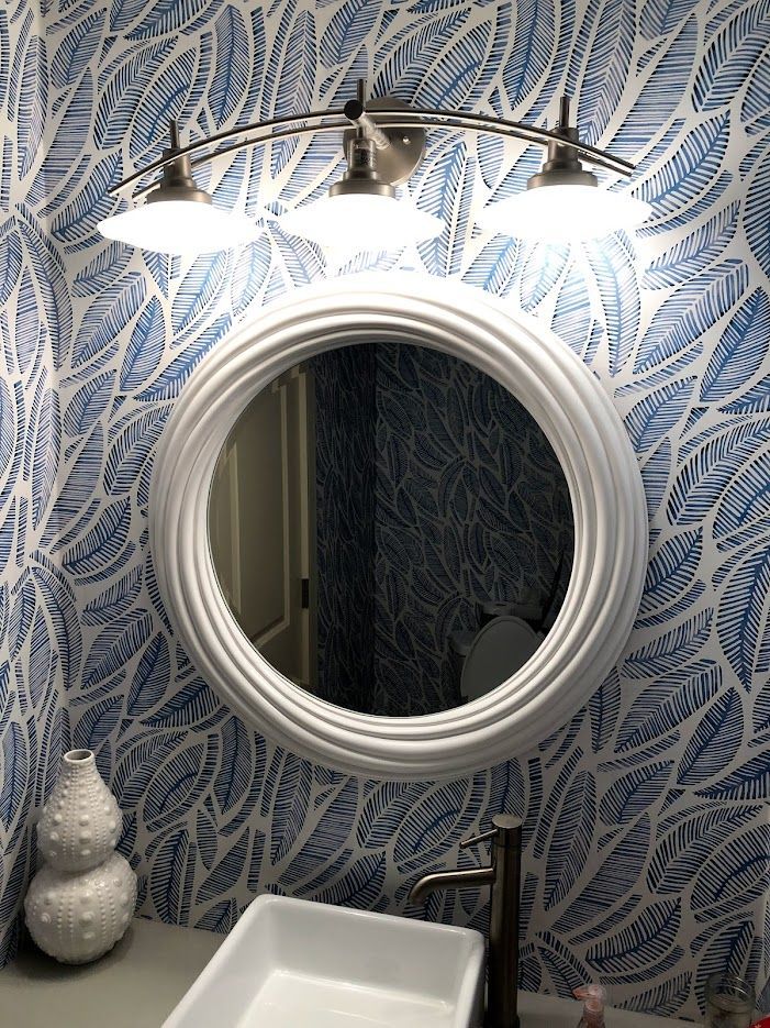 Bathroom with white round mirror, blue patterned wallpaper, and sink.
