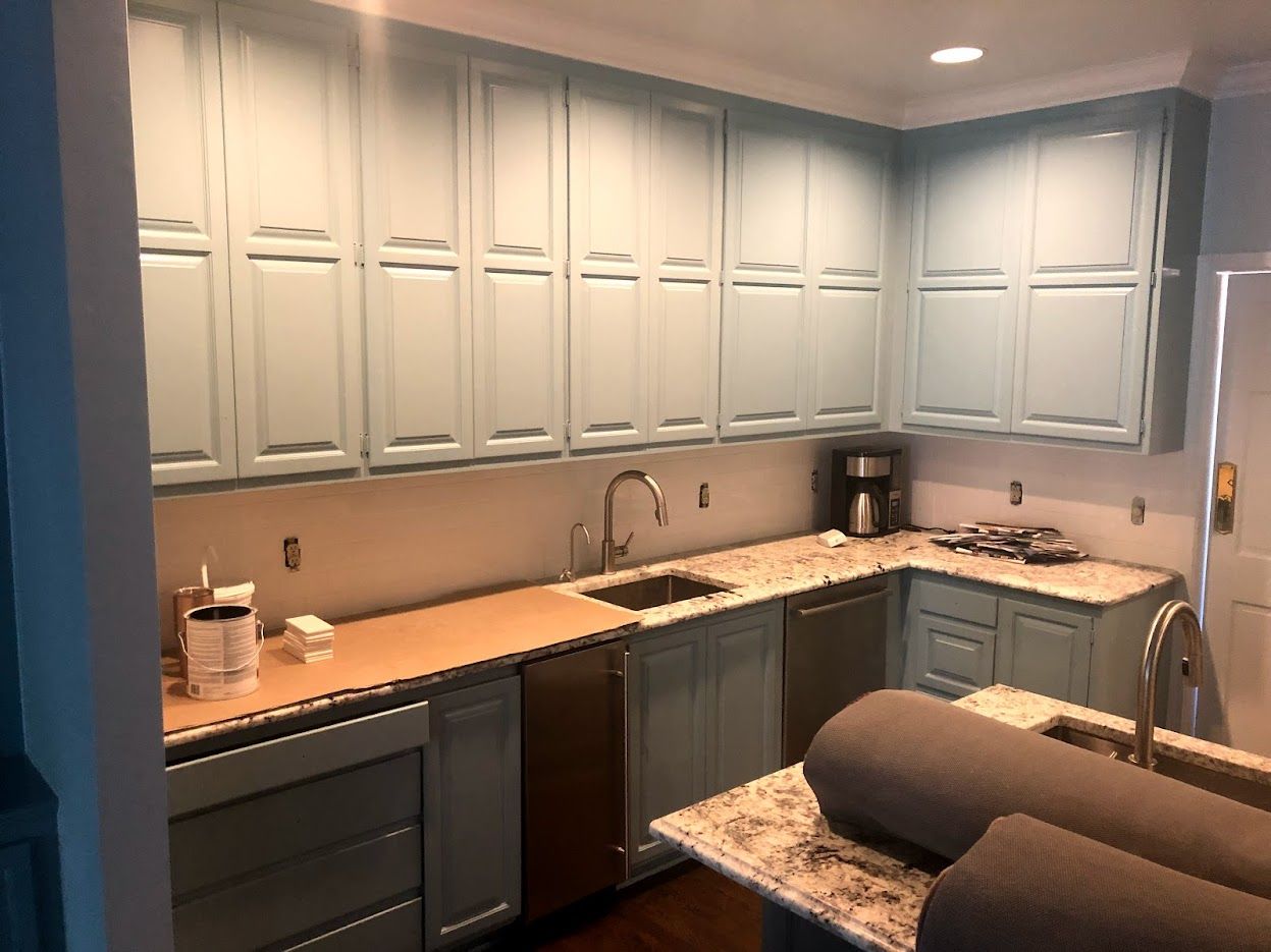 A kitchen with blue cabinets , granite counter tops , stainless steel appliances and a sink.