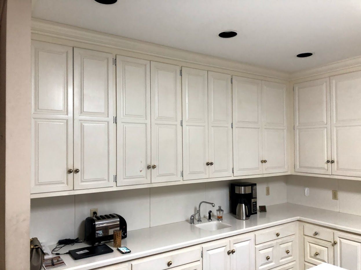 White kitchen cabinets and countertops with appliances, sink, and recessed lighting.