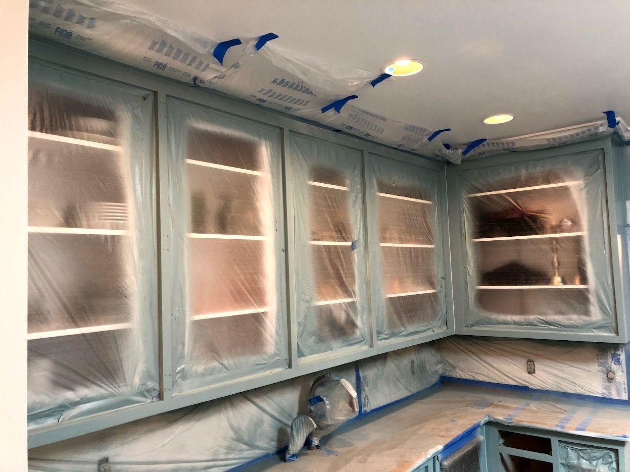 Kitchen cabinets, painted light blue, covered in plastic for protection during a renovation.