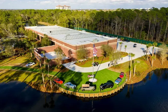 Building with American flag and cars on a grassy point, surrounded by water and trees.