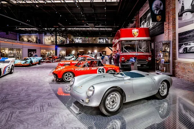 Silver Porsche 550 Spyder in a museum with other classic cars and a red double-decker bus.