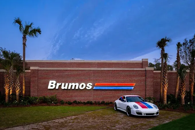 Brumos sign with a white Porsche sports car displaying the team's signature red, blue, and orange stripes.