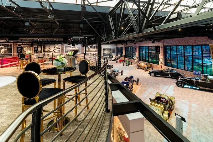 Interior view of a car museum with vintage vehicles and a balcony with bar stools.