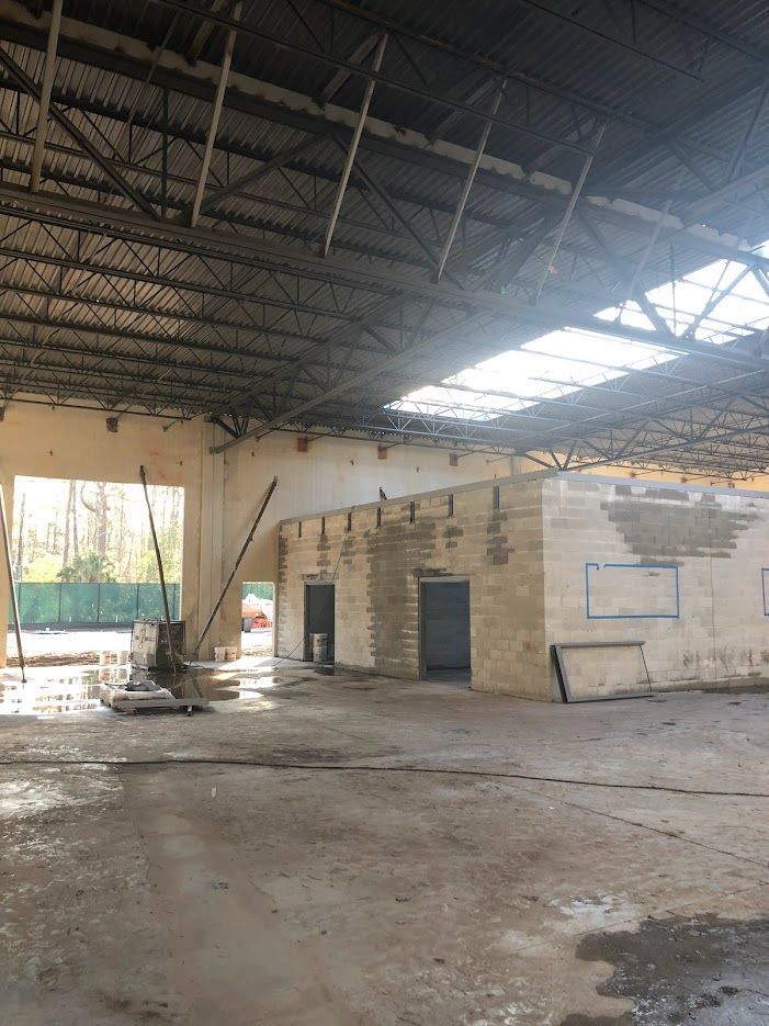 Inside a large, empty warehouse with water on the floor. Metal braces support a long wall.
