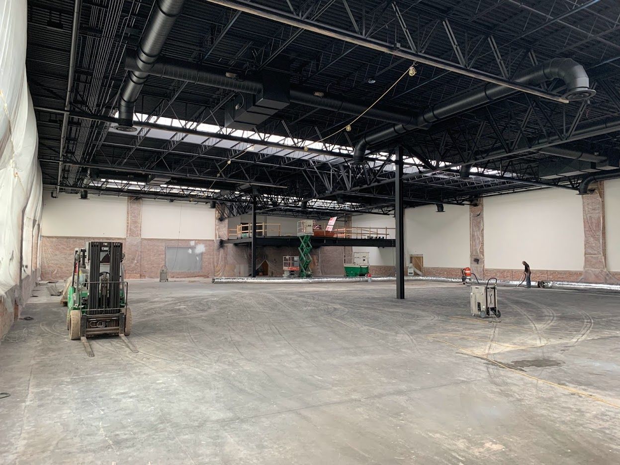 An empty warehouse under construction, black ceiling, forklift, brick accents, and workers.