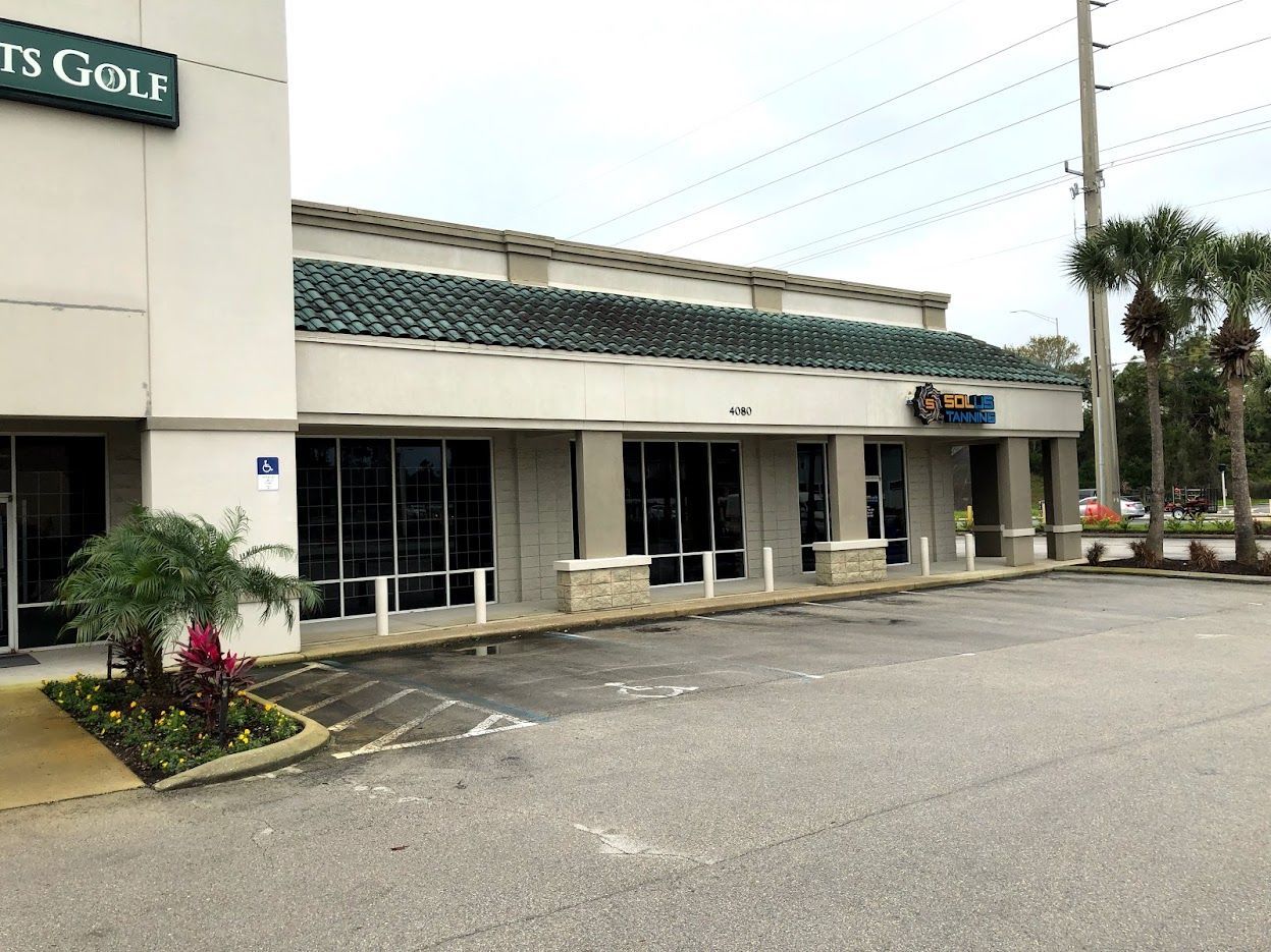 Exterior view of a strip mall with storefronts, asphalt parking lot, and a cloudy sky.