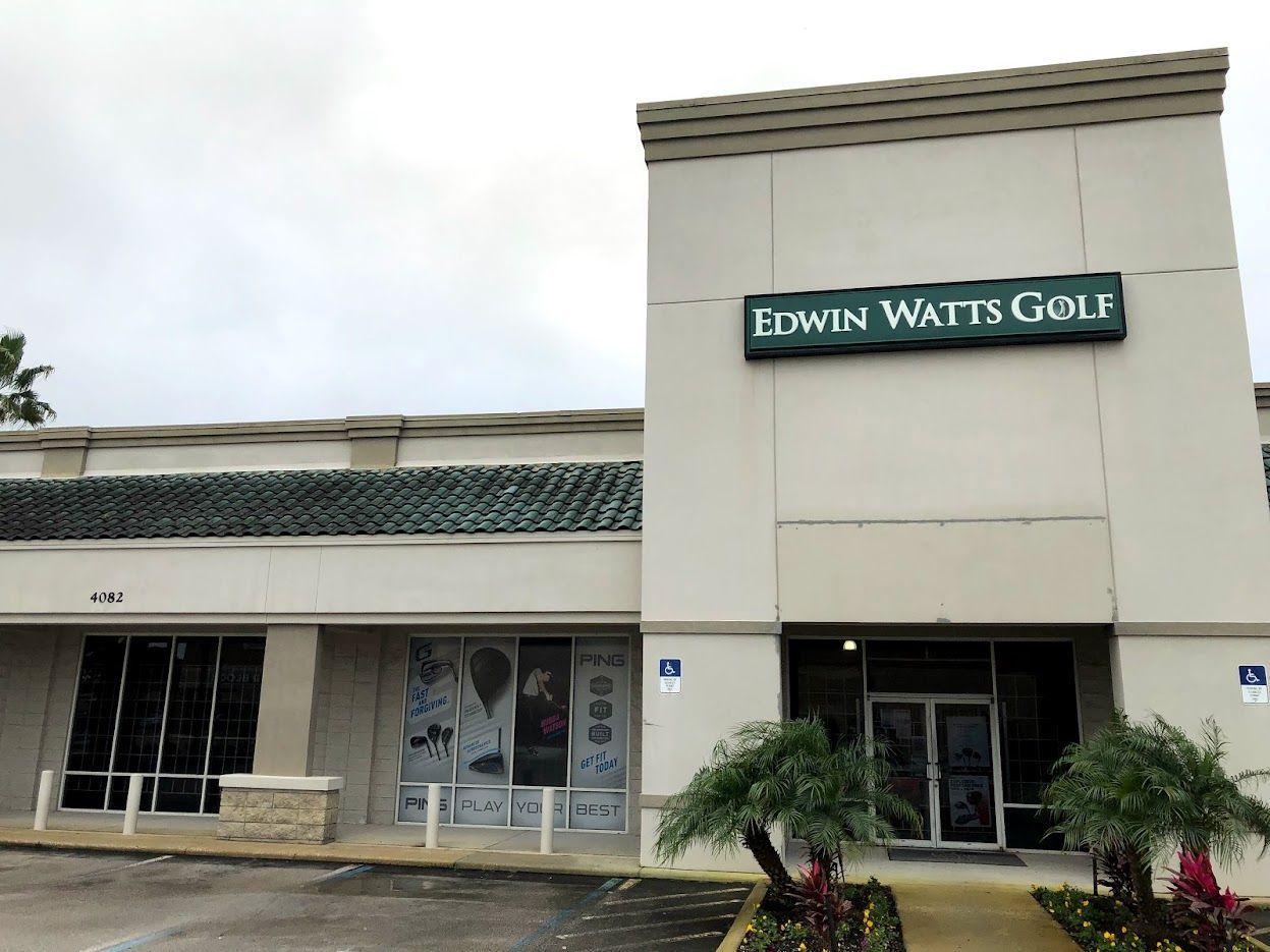 Exterior view of Edwin Watts Golf store; light-colored building with green sign and entrance, palm trees.