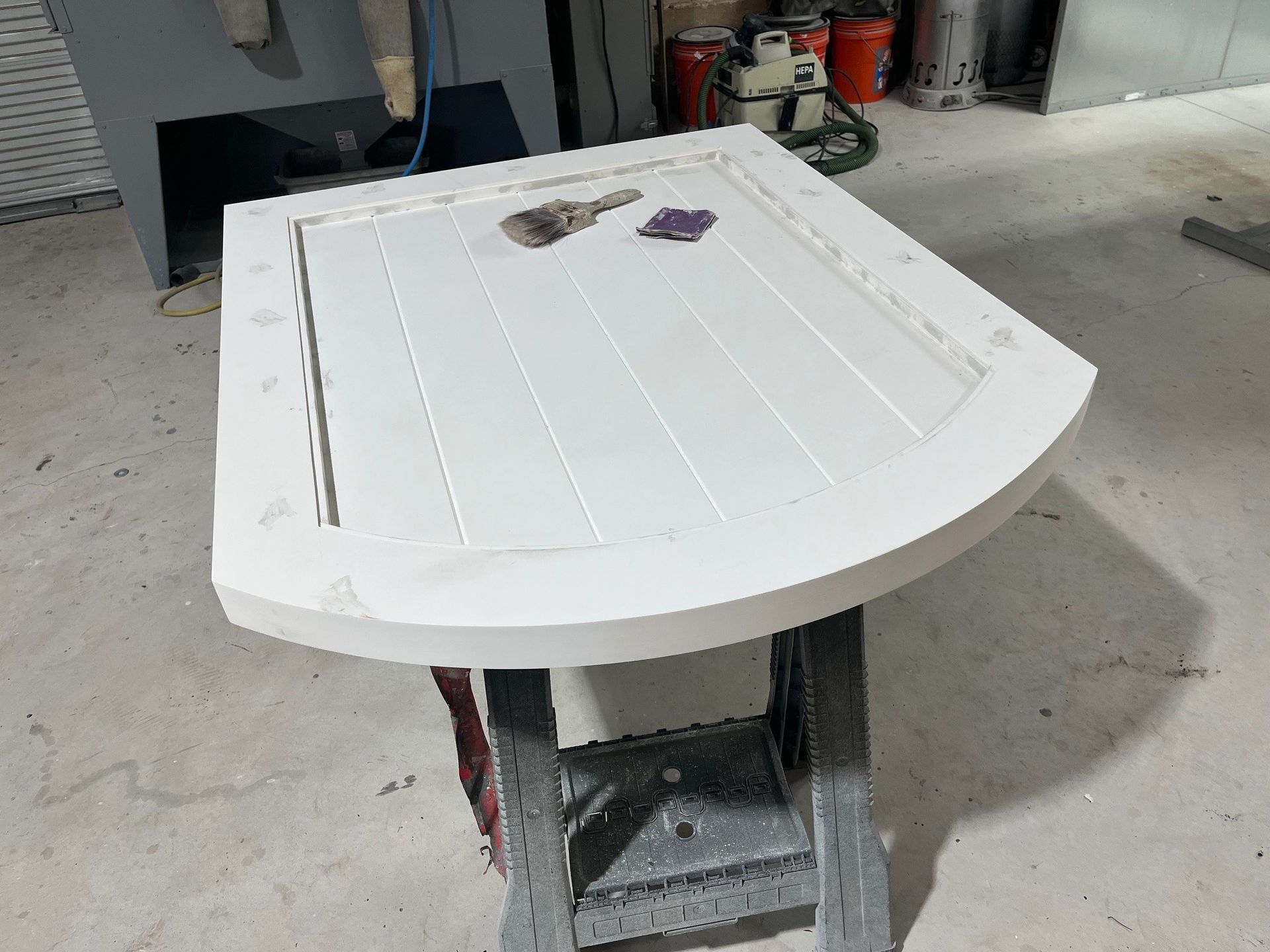 White, semi-circular shower door on a workbench. The door has ribbed details and a curved edge.