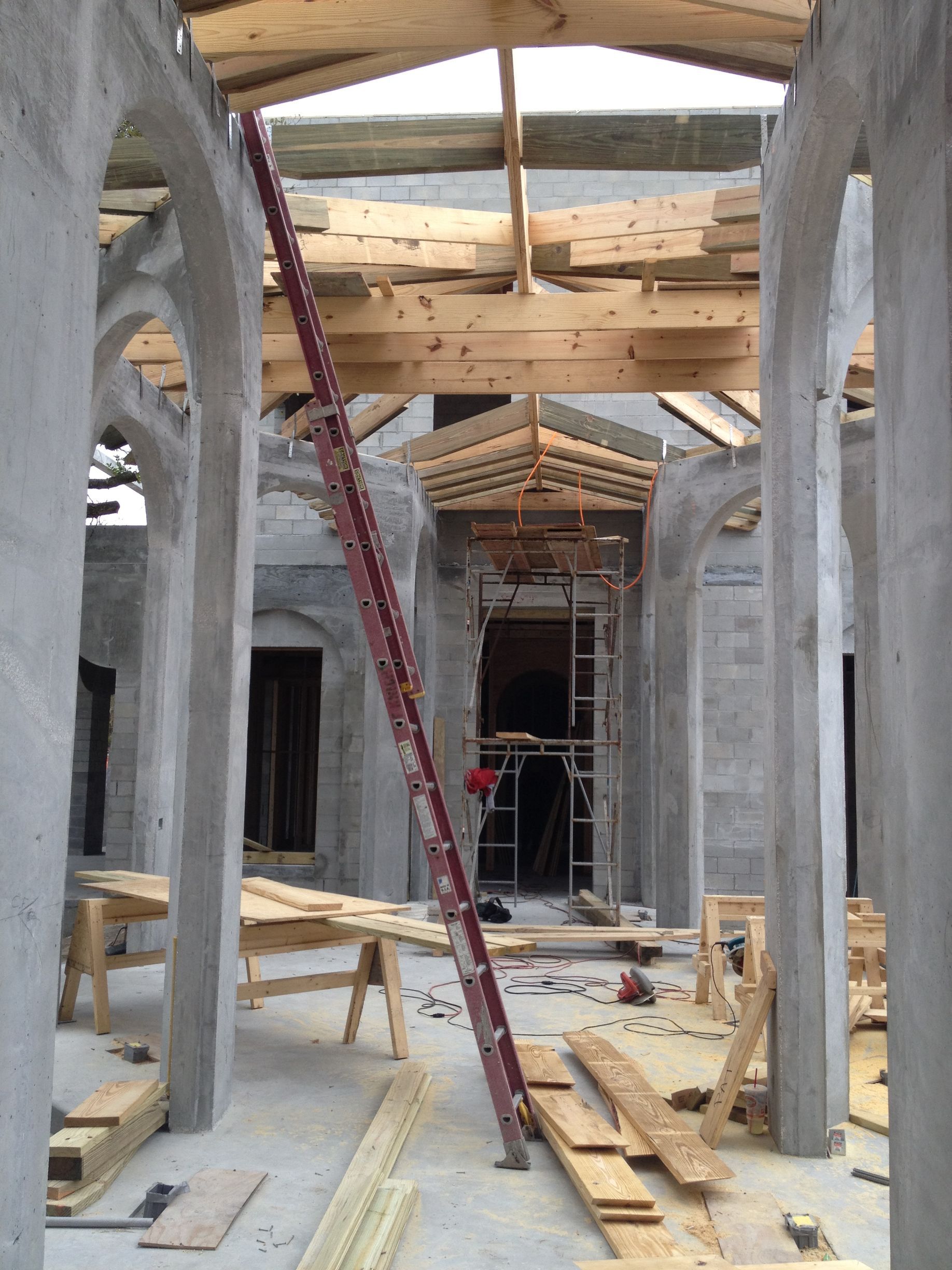 Interior of a building under construction, showing arches, wooden beams, and a ladder.