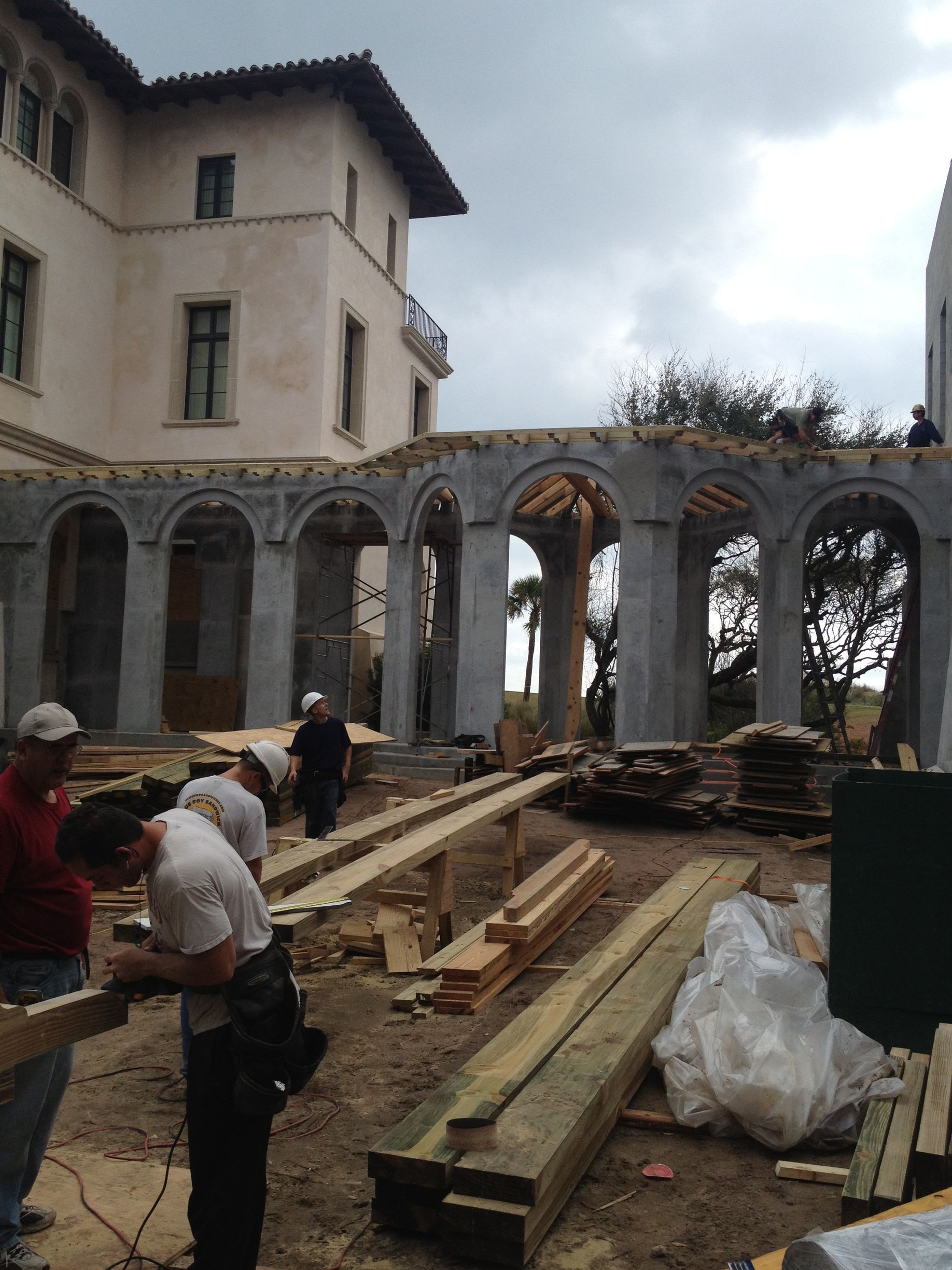 Construction workers building a structure with arched columns next to a large building.