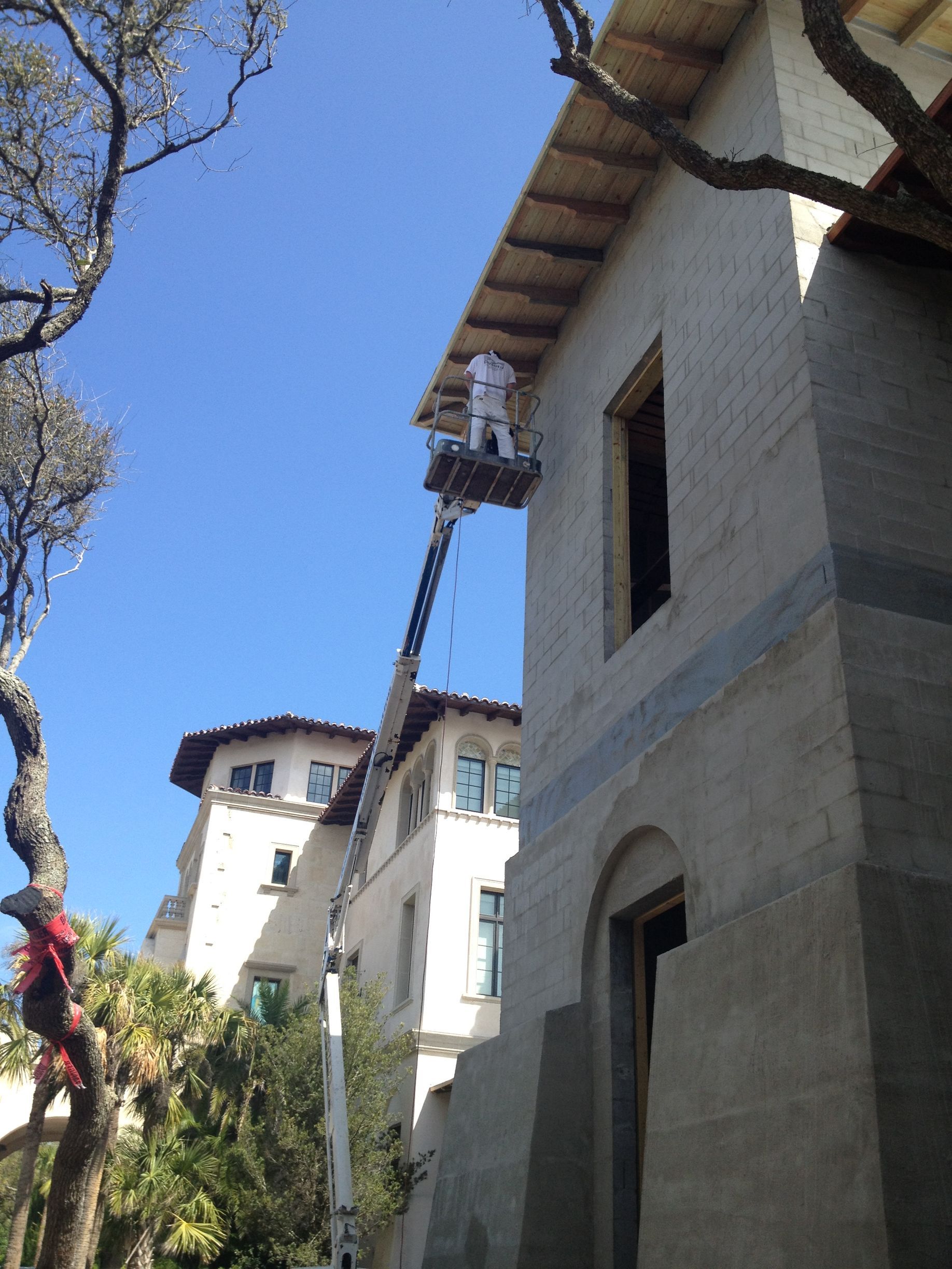 Person in lift working on the exterior of a two-story building on a sunny day.