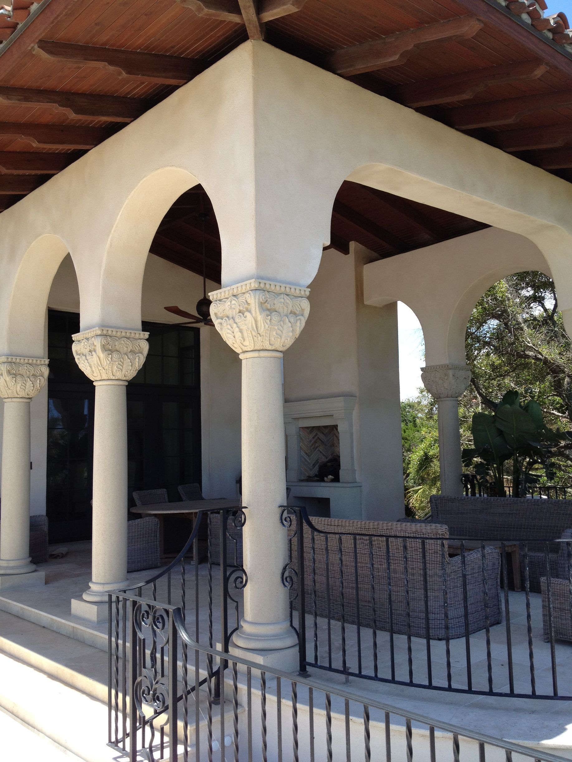 Outdoor covered patio with arched openings and decorative columns, a fireplace, and wrought iron railing.