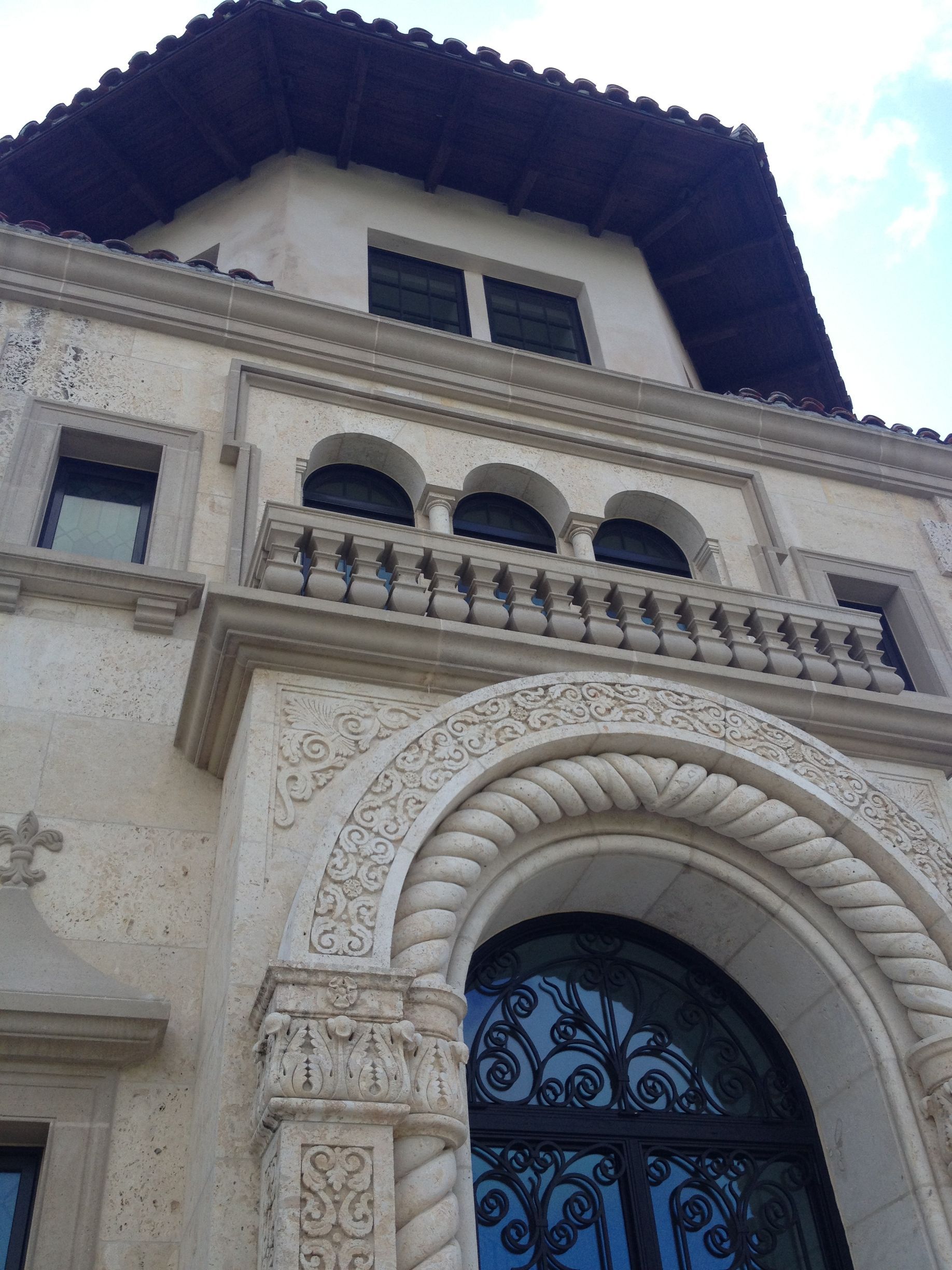 Beige stone building with arched windows, balcony, and ornate details under a dark tiled roof.