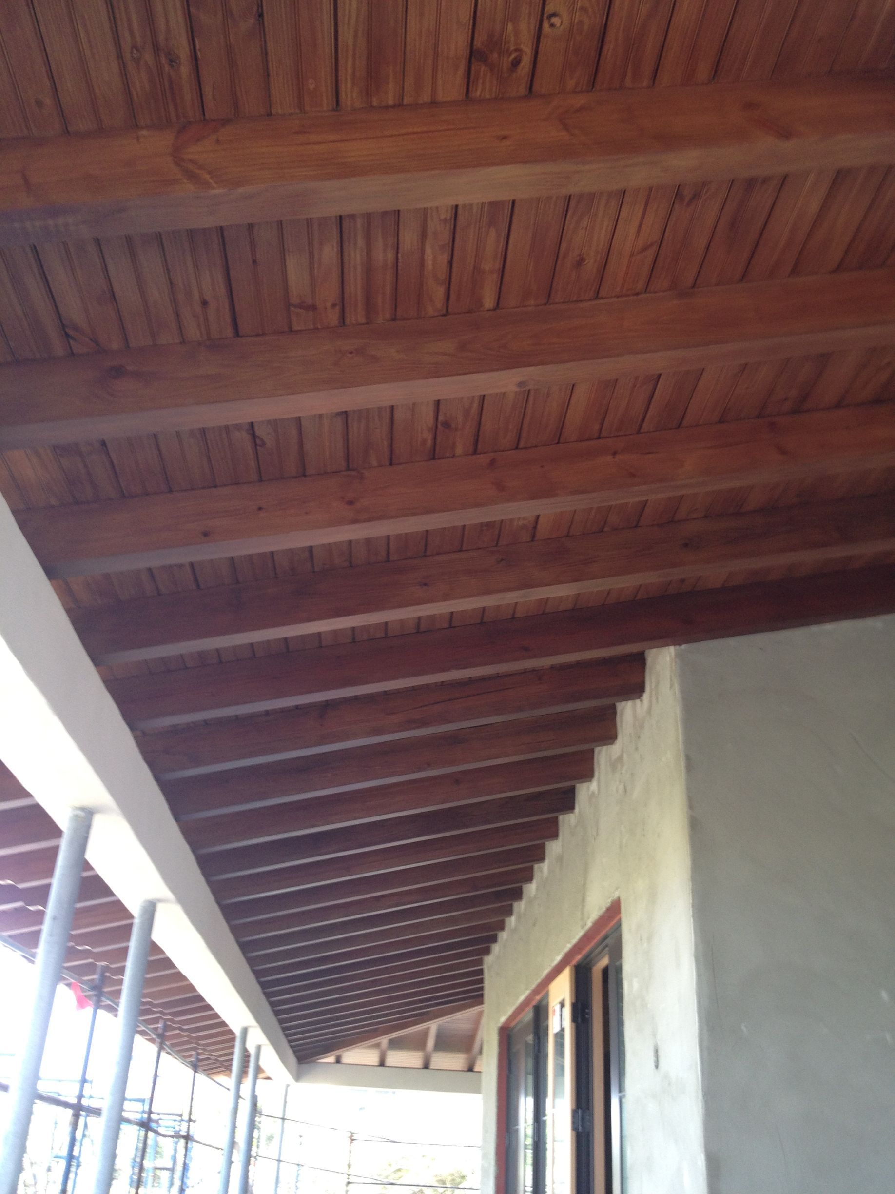 Wooden ceiling with exposed beams, extending from a building's exterior.