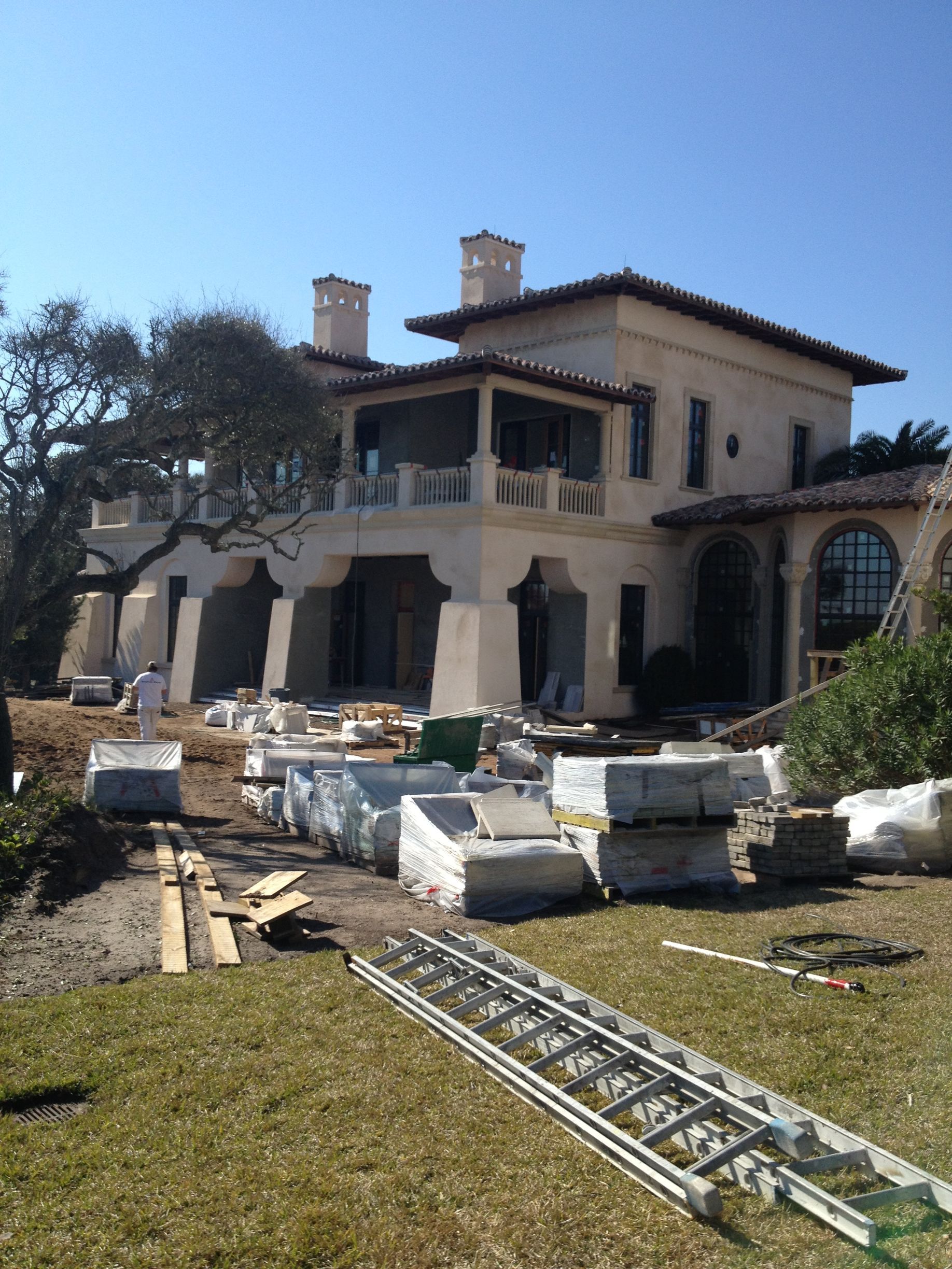Large beige house under construction; materials and ladder in yard.