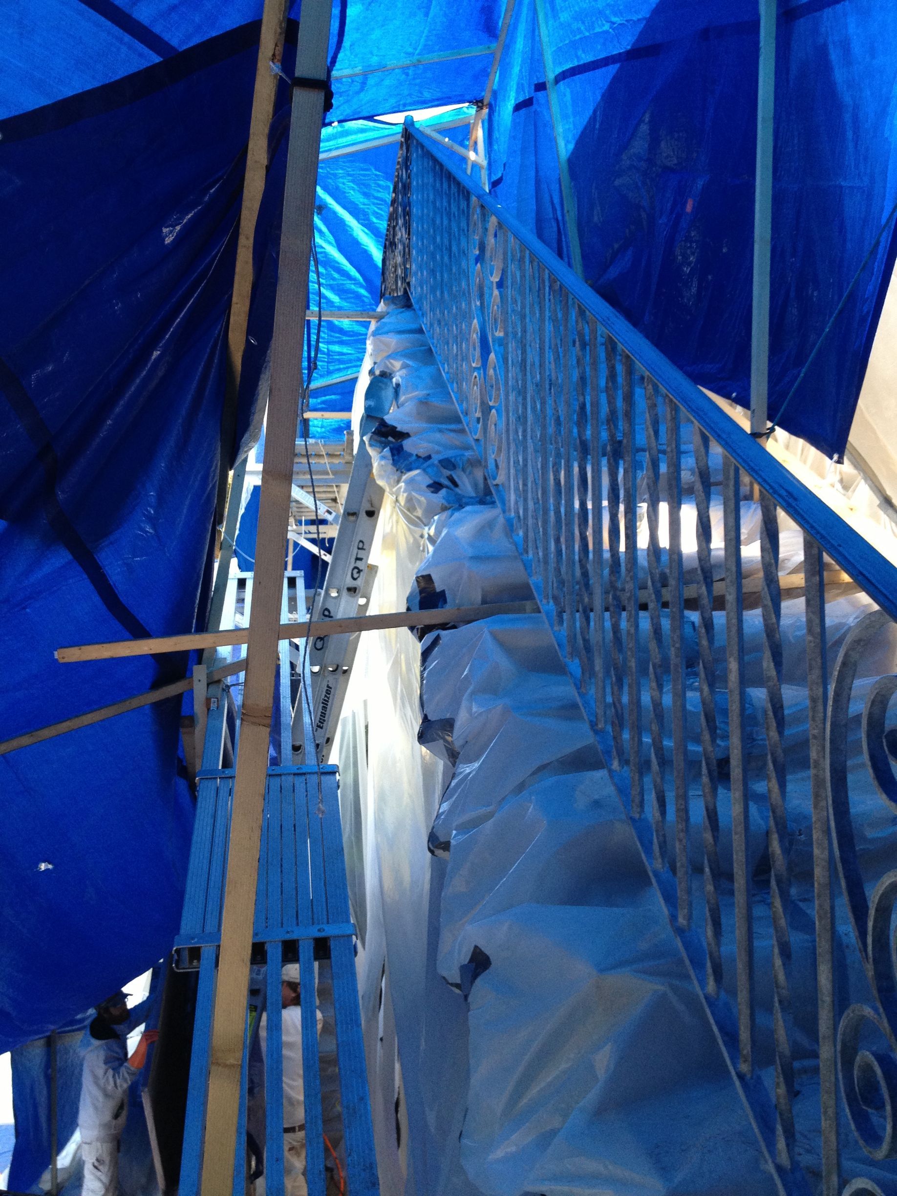 Blue tarp covers scaffolding and stairs. Metal railing on the stairs.