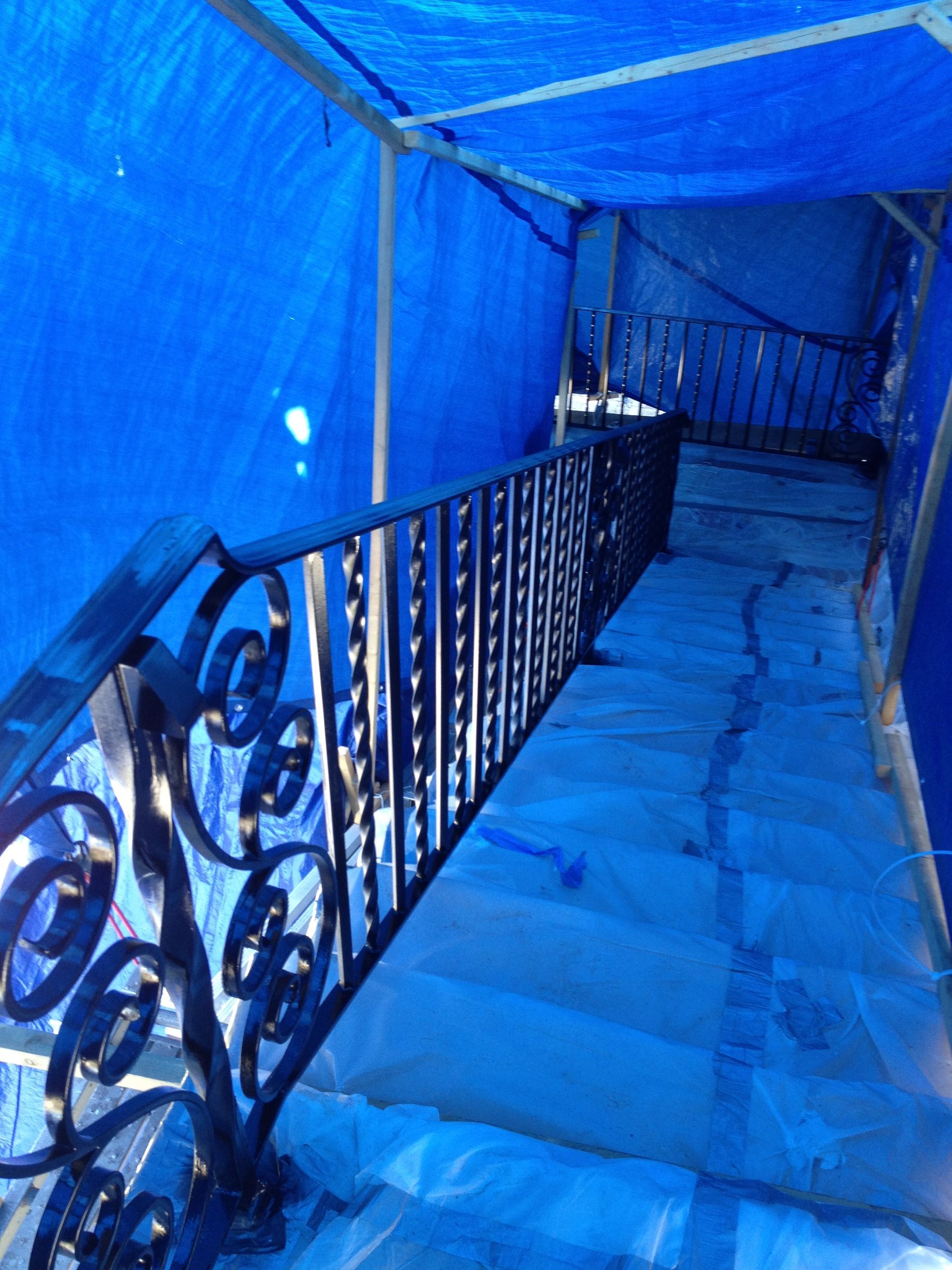 Black wrought iron stair railing on steps covered with protective blue tarp.