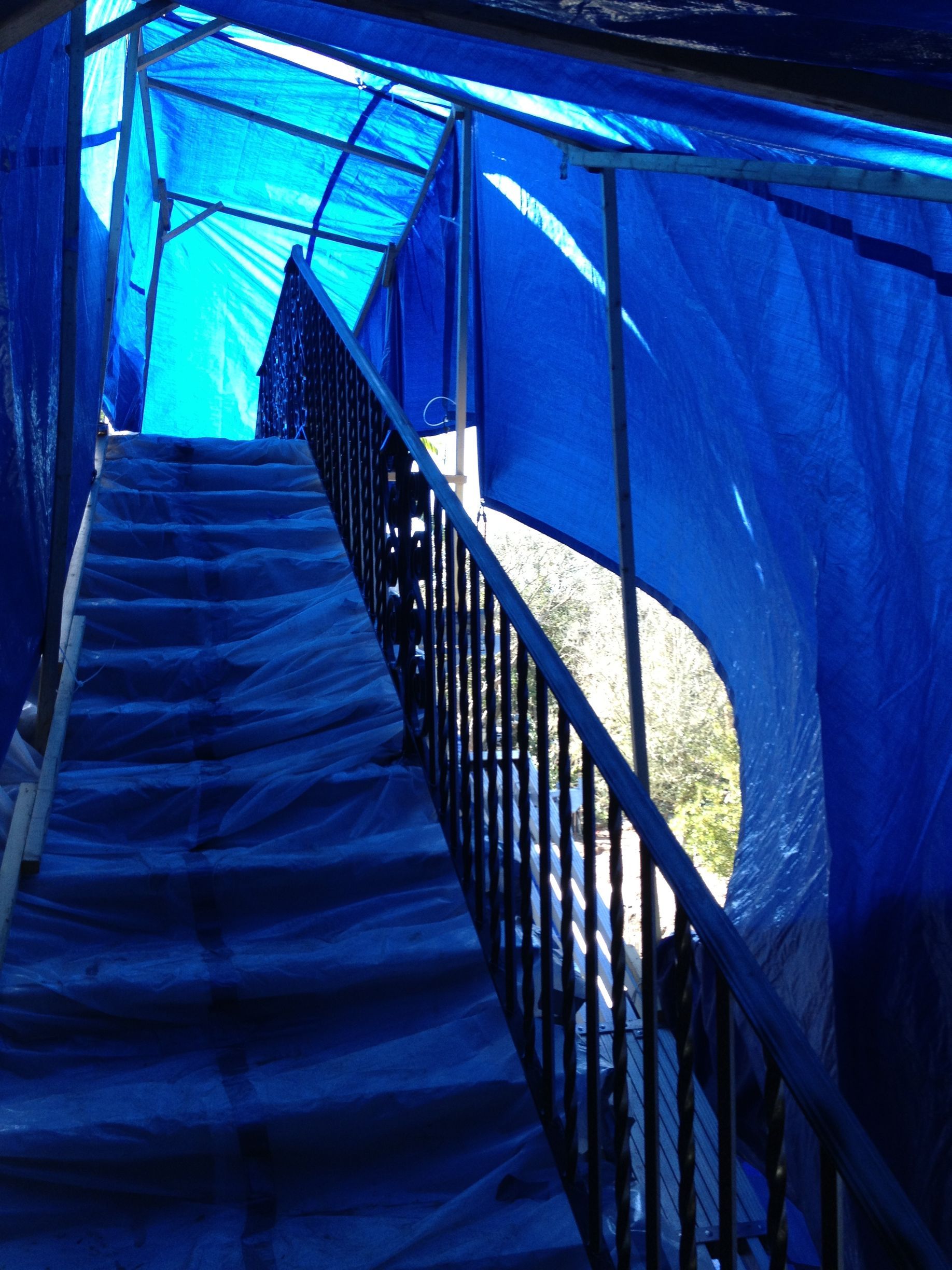 Staircase covered in blue tarps with a black railing, leading upwards.