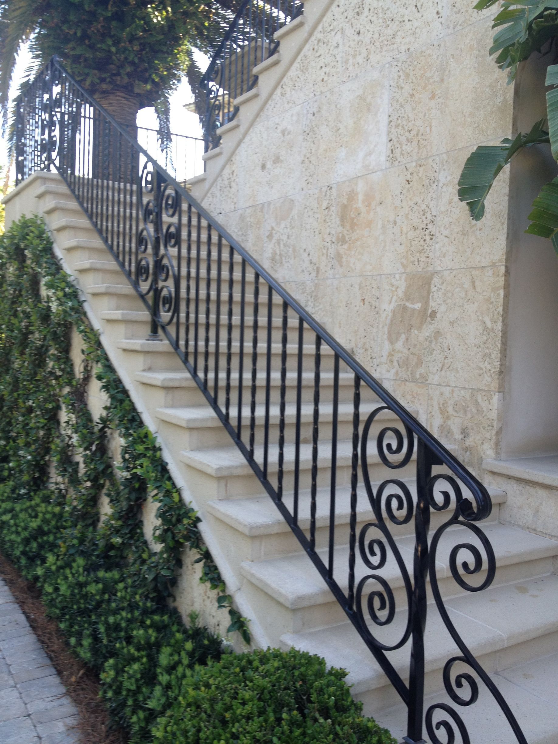 Stone stairs with black wrought iron railing, climbing a wall with growing ivy and plants.