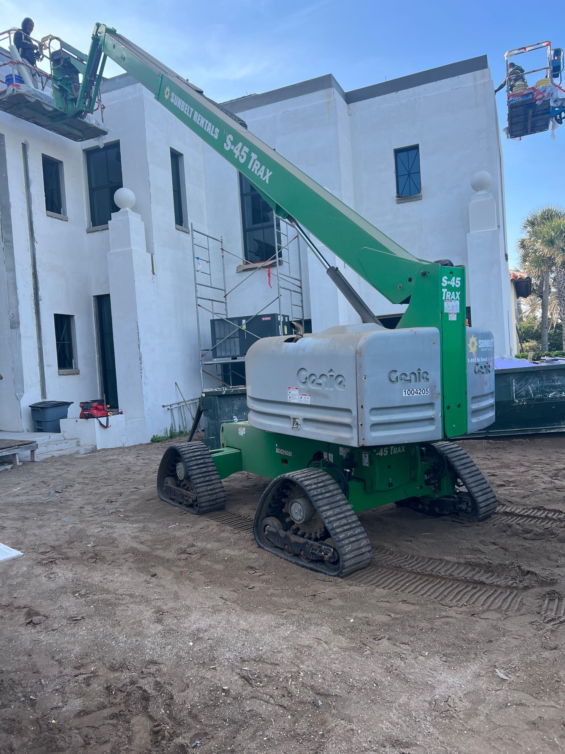 A green Genie S-45 XC boom lift next to a white building under construction. Workers are visible on the roof.
