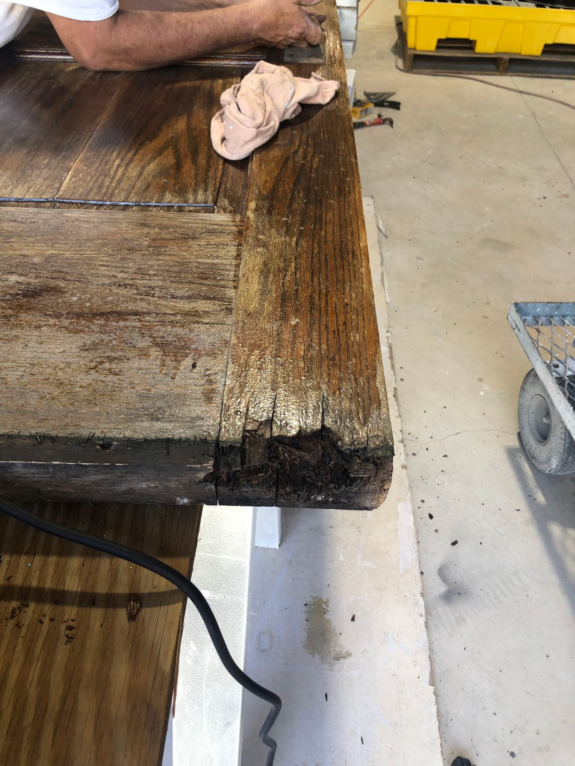 Person wiping a weathered wooden surface, possibly restoring furniture in a workshop.