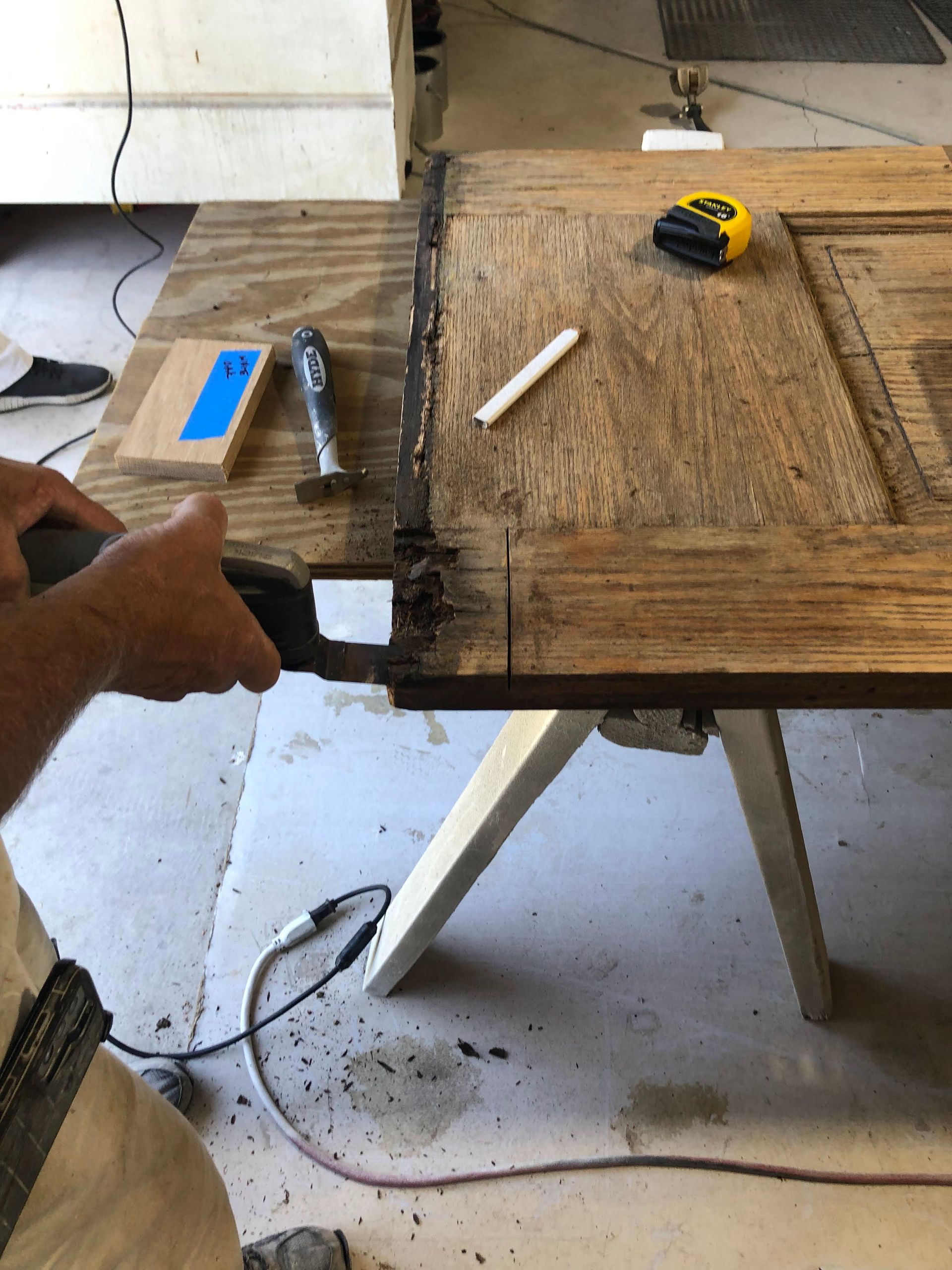 Person cutting door on a workbench with a saw, measuring tape, and chalk.