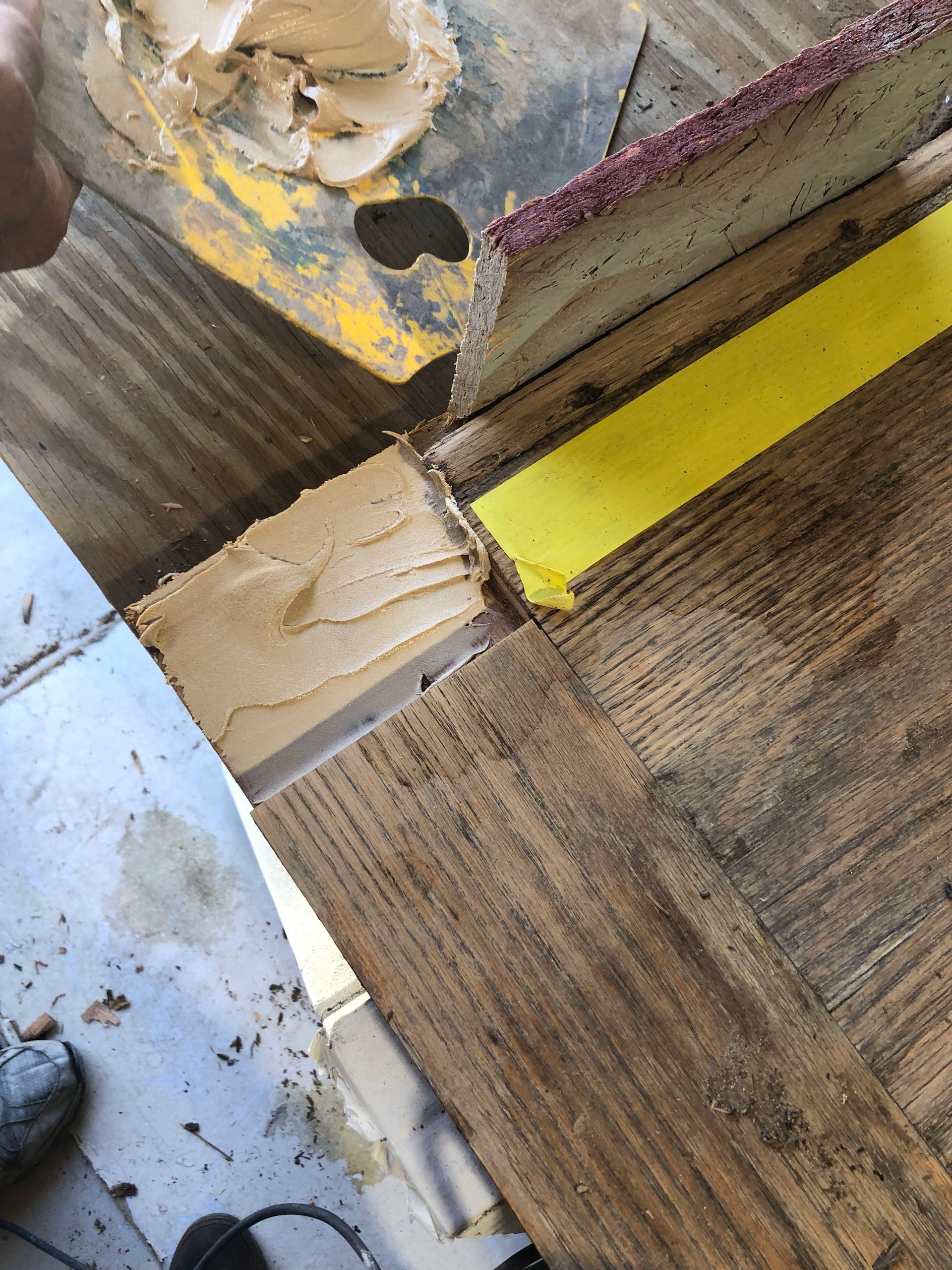 Wood repair: Putty being applied to a wood joint with yellow and purple sanding tools, in a wooden setting.