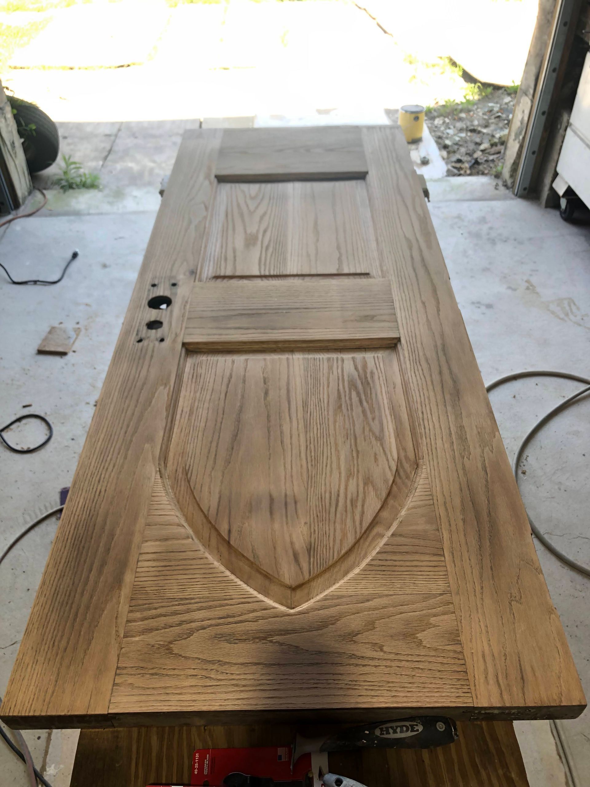 Wooden door with shield-shaped panel and two rectangular panels on a workbench.