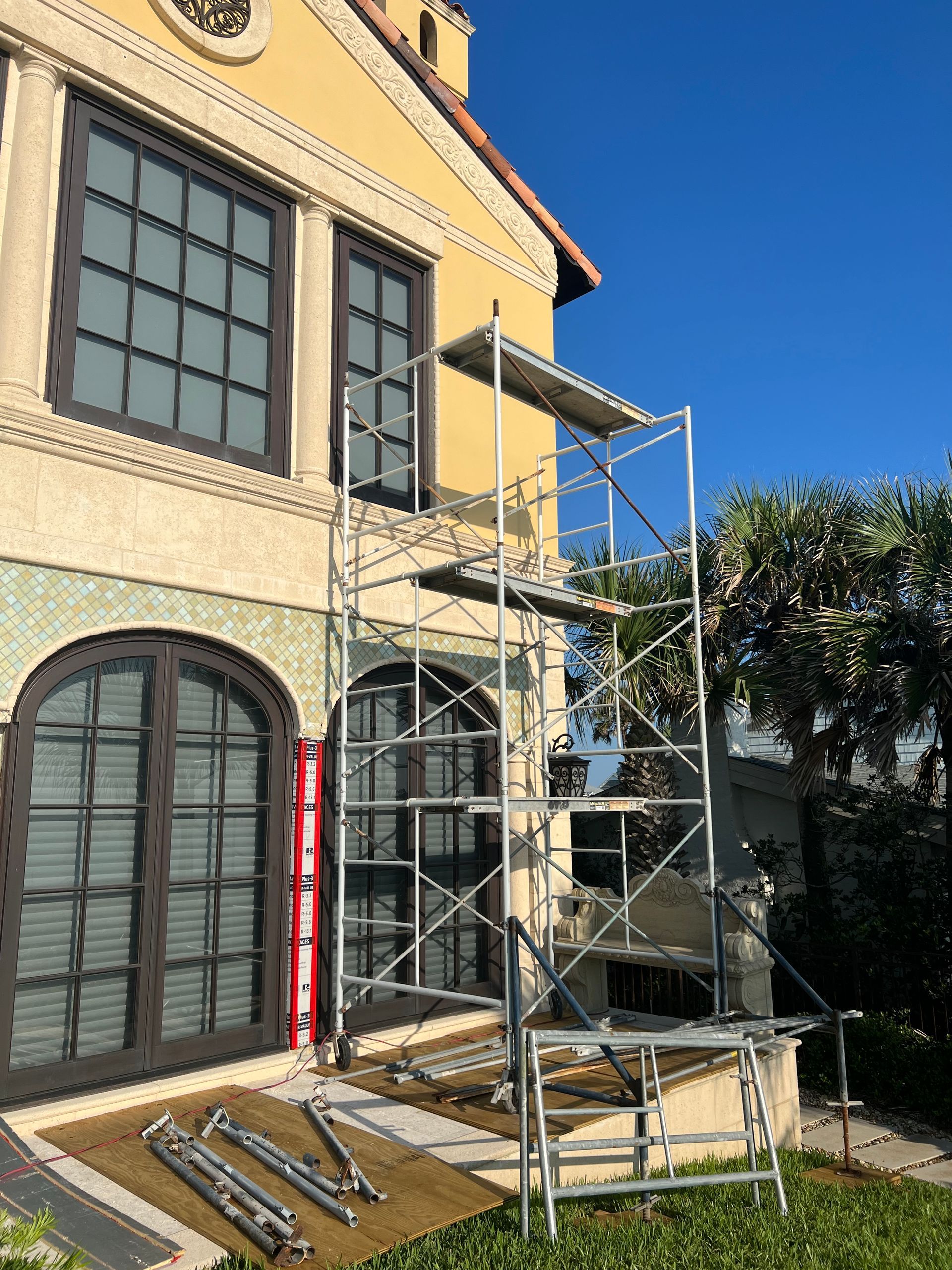 Scaffolding erected next to a building with dark-framed windows and doors.