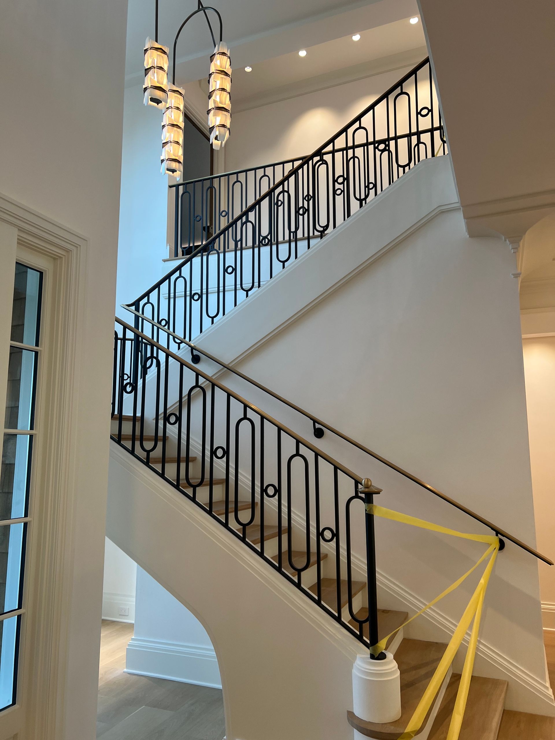 Staircase with black wrought iron railing, beige walls, and a hanging light fixture.