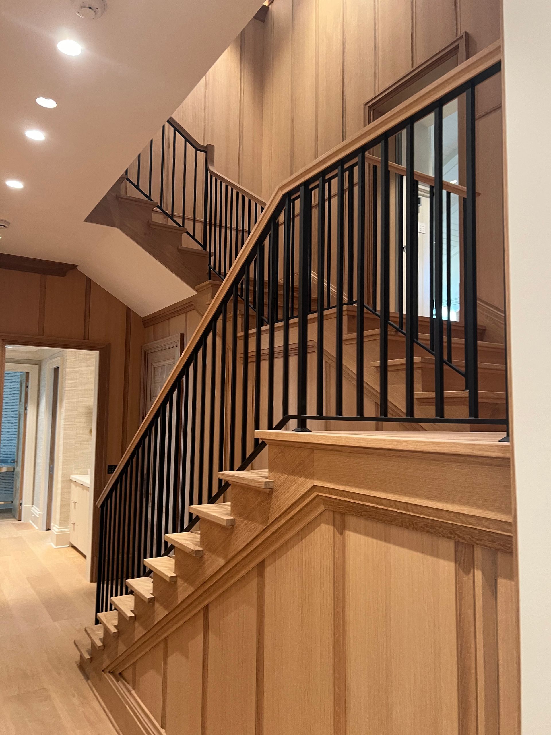 Wooden staircase with black railing and paneled walls.
