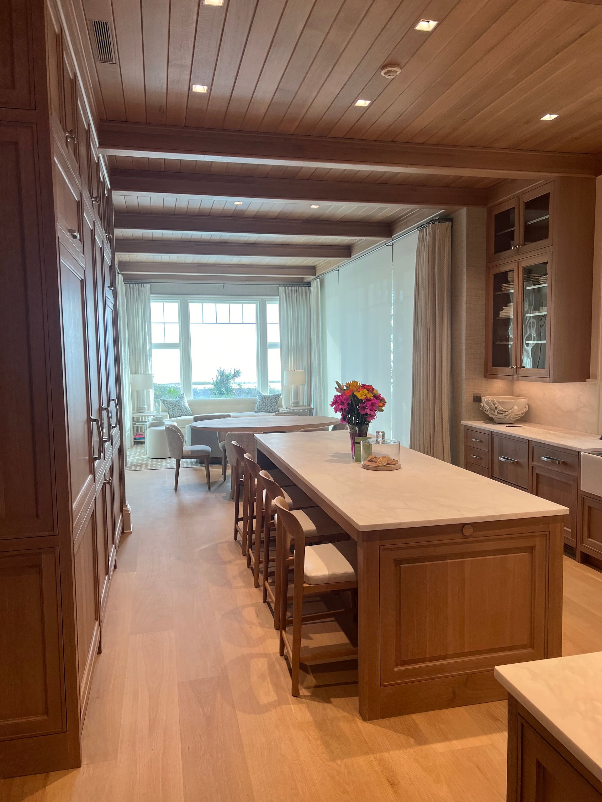 Wooden kitchen with an island, cabinets, and beamed ceiling; a breakfast nook is visible through the window.