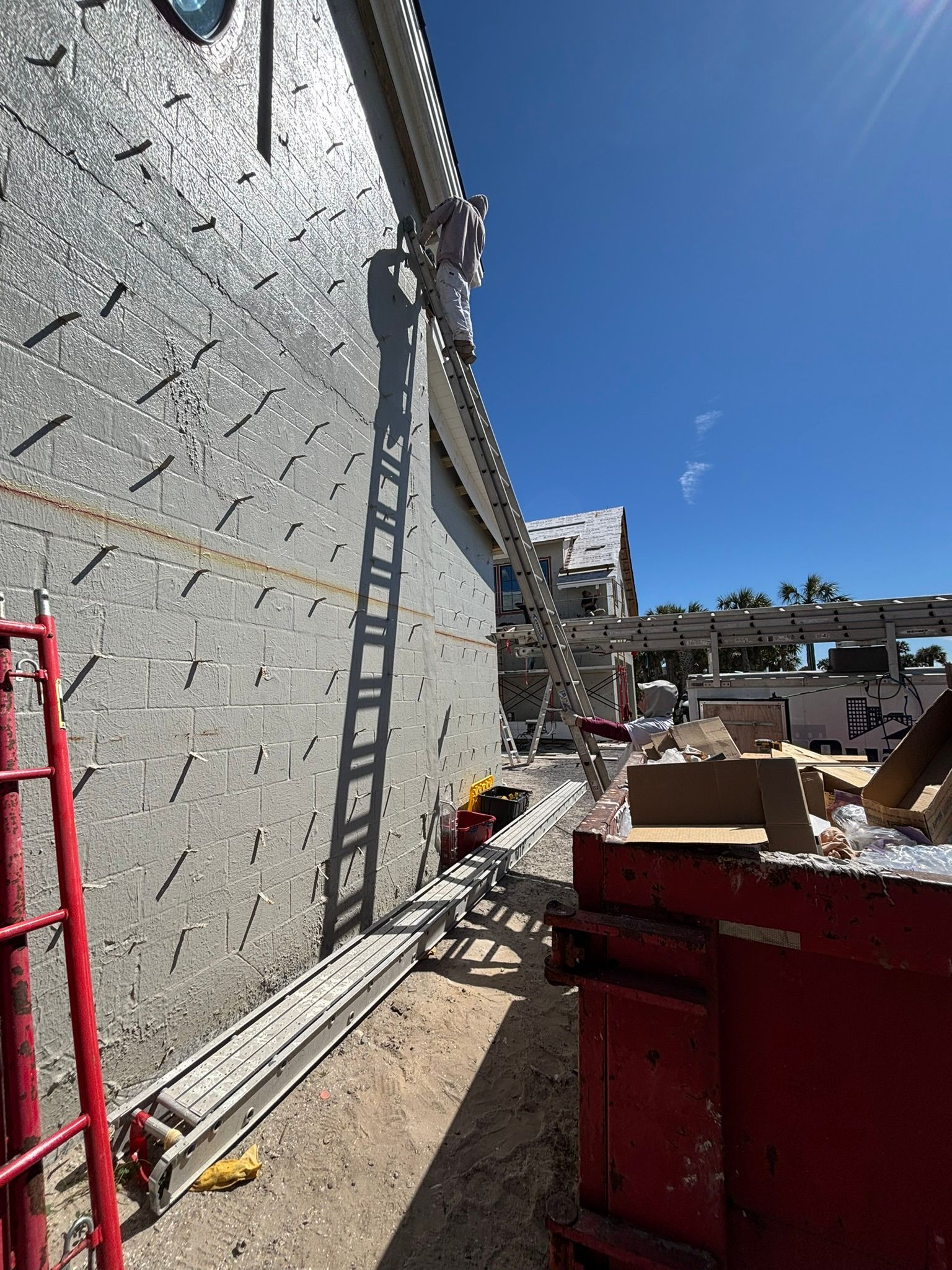 Construction worker on ladder, repairing building exterior with scaffolding and debris in the background.