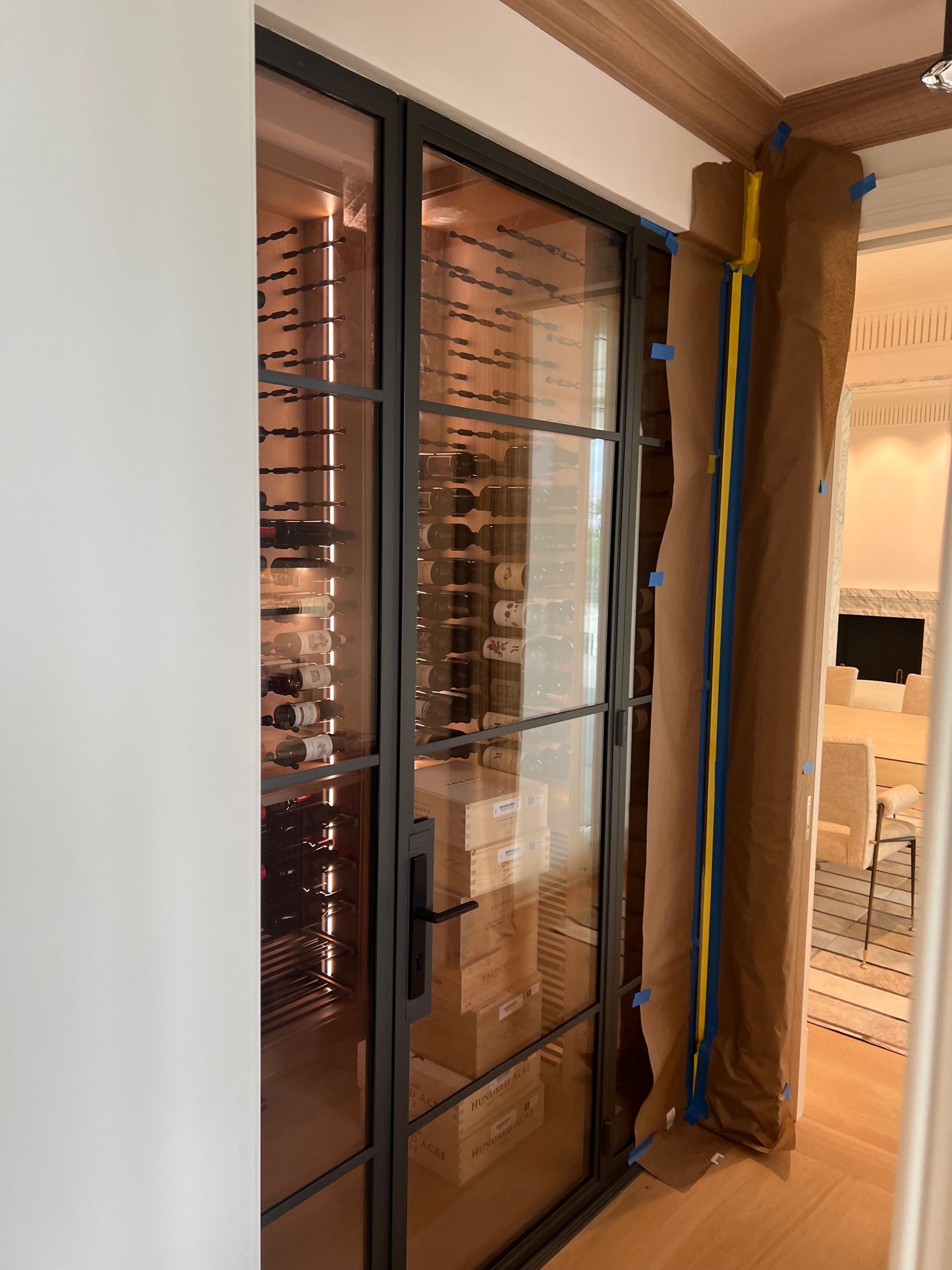 Black framed glass wine cellar door. Interior view with wine bottles visible inside.