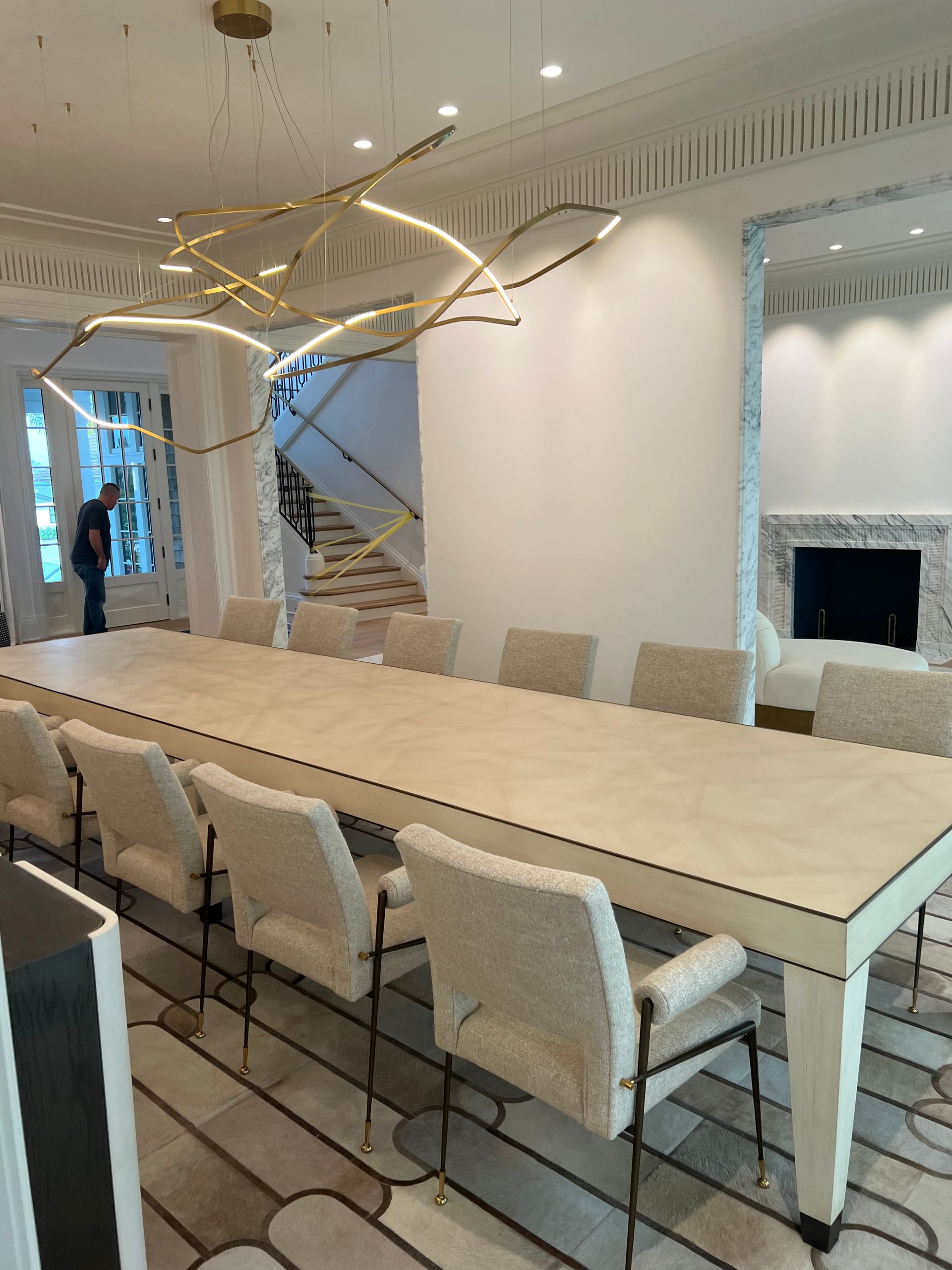 A long dining table with 12 chairs beneath a modern chandelier in a luxurious dining room.