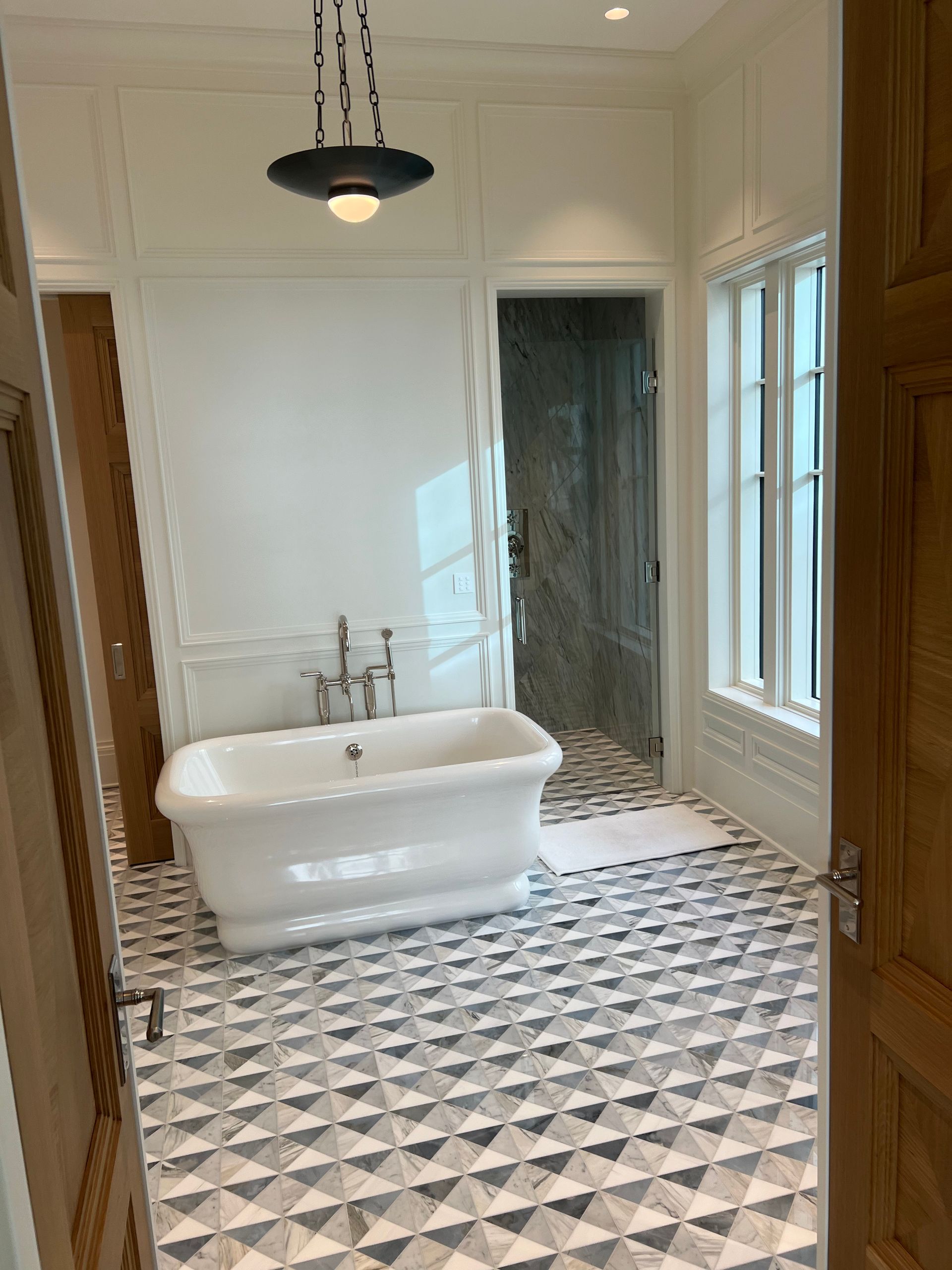 Bathroom with a white clawfoot tub, geometric tile floor, and a hanging light.