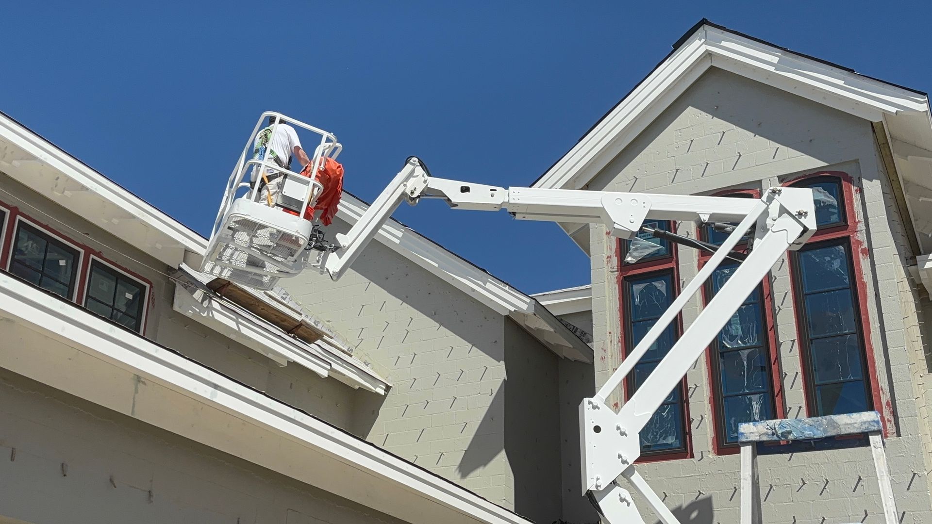 Construction worker on a ladder by a building. Bright blue sky, red ladder, gray wall.