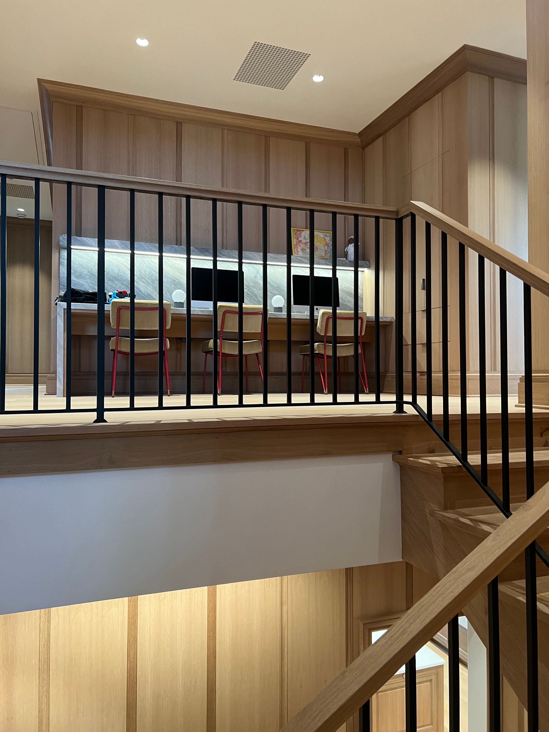 Wooden staircase with black railing, leading to a mezzanine with workspace and desks.