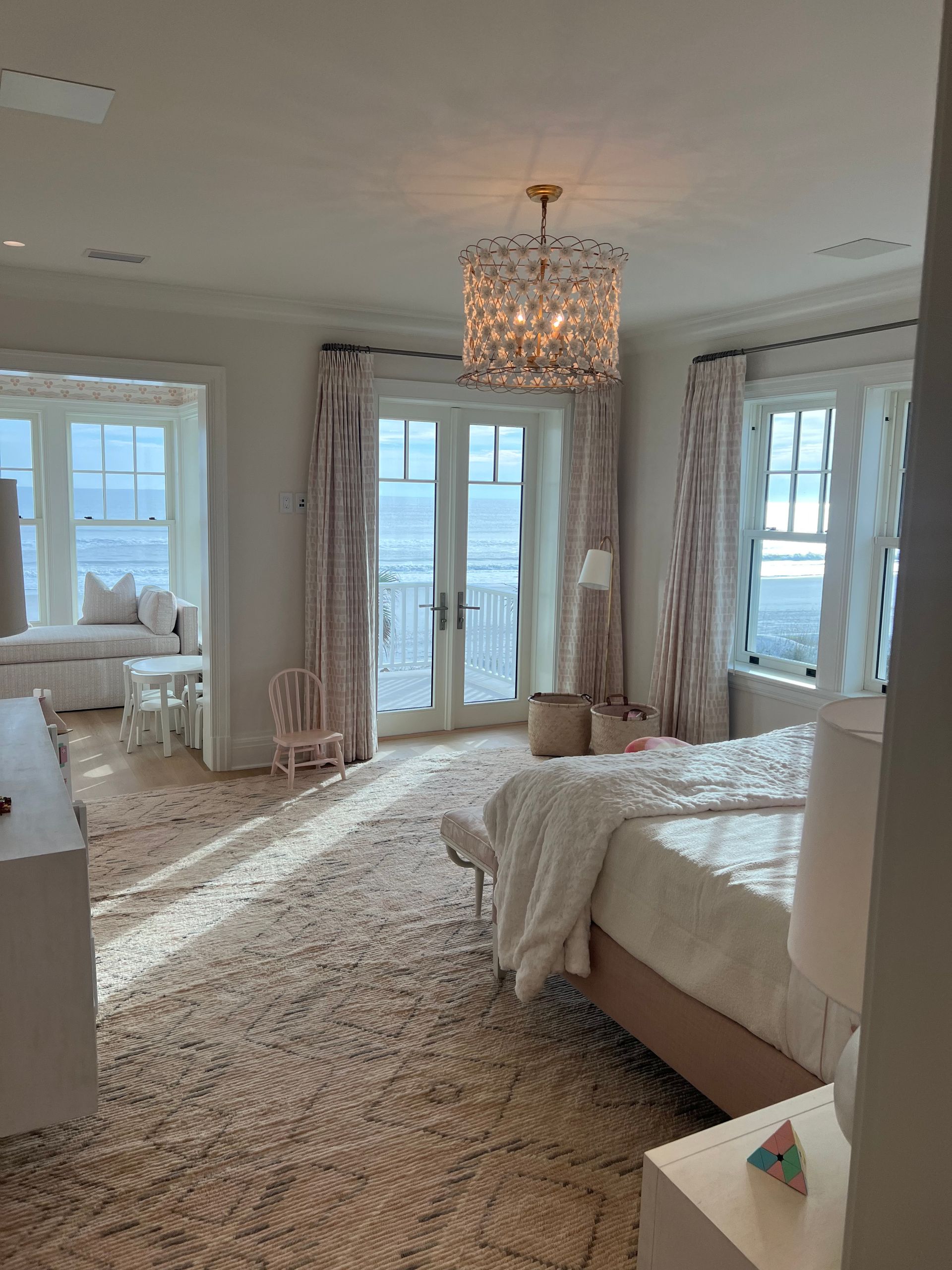 Spacious bedroom with ocean view, pink rug, chandelier, windows, and bed.