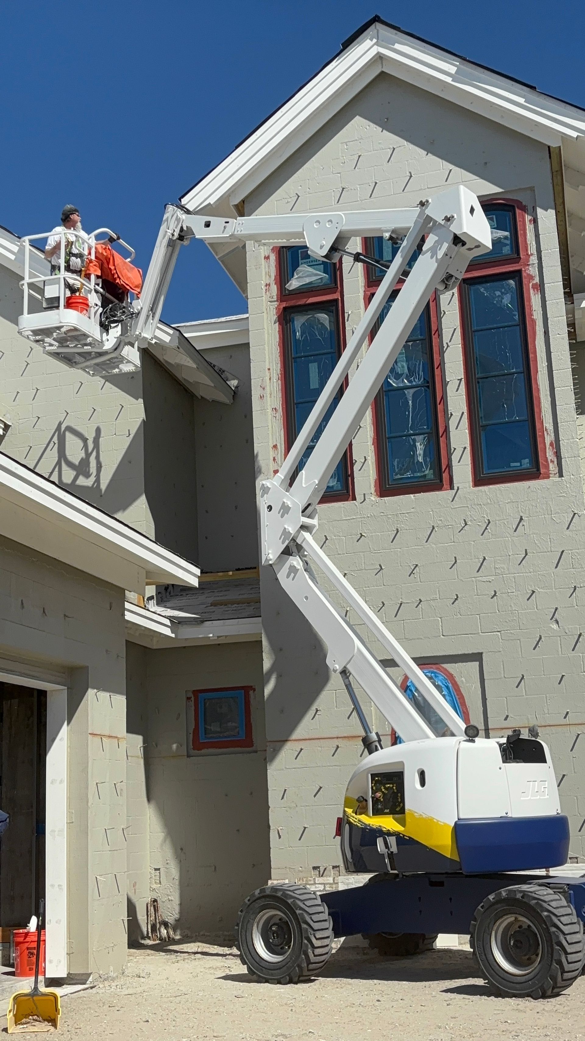 Construction worker in an orange vest on an aerial lift working on a two-story stucco building.