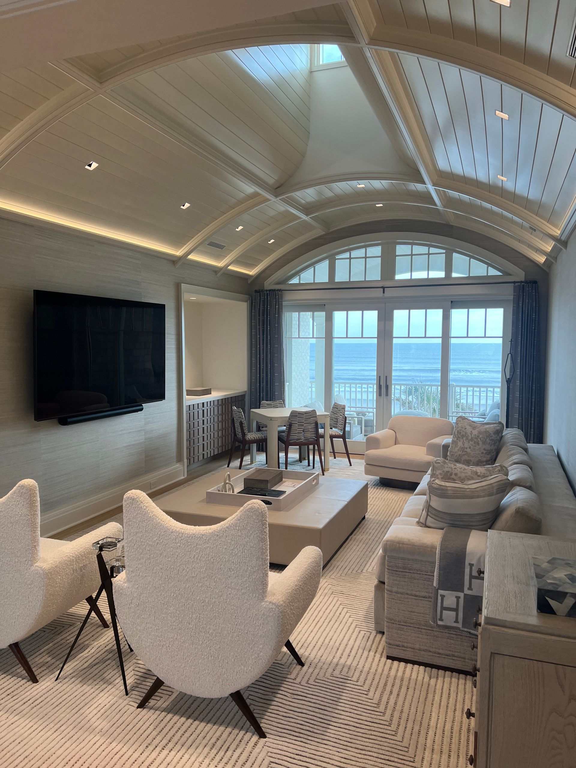 Living room with white and neutral tones, large windows, sofa, and chairs.