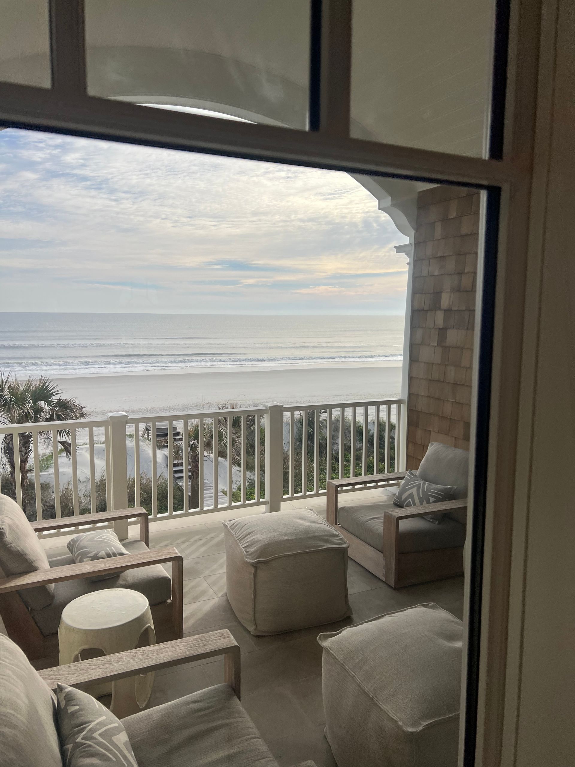 Ocean view from a porch with outdoor furniture: chairs, ottomans, and a small table.