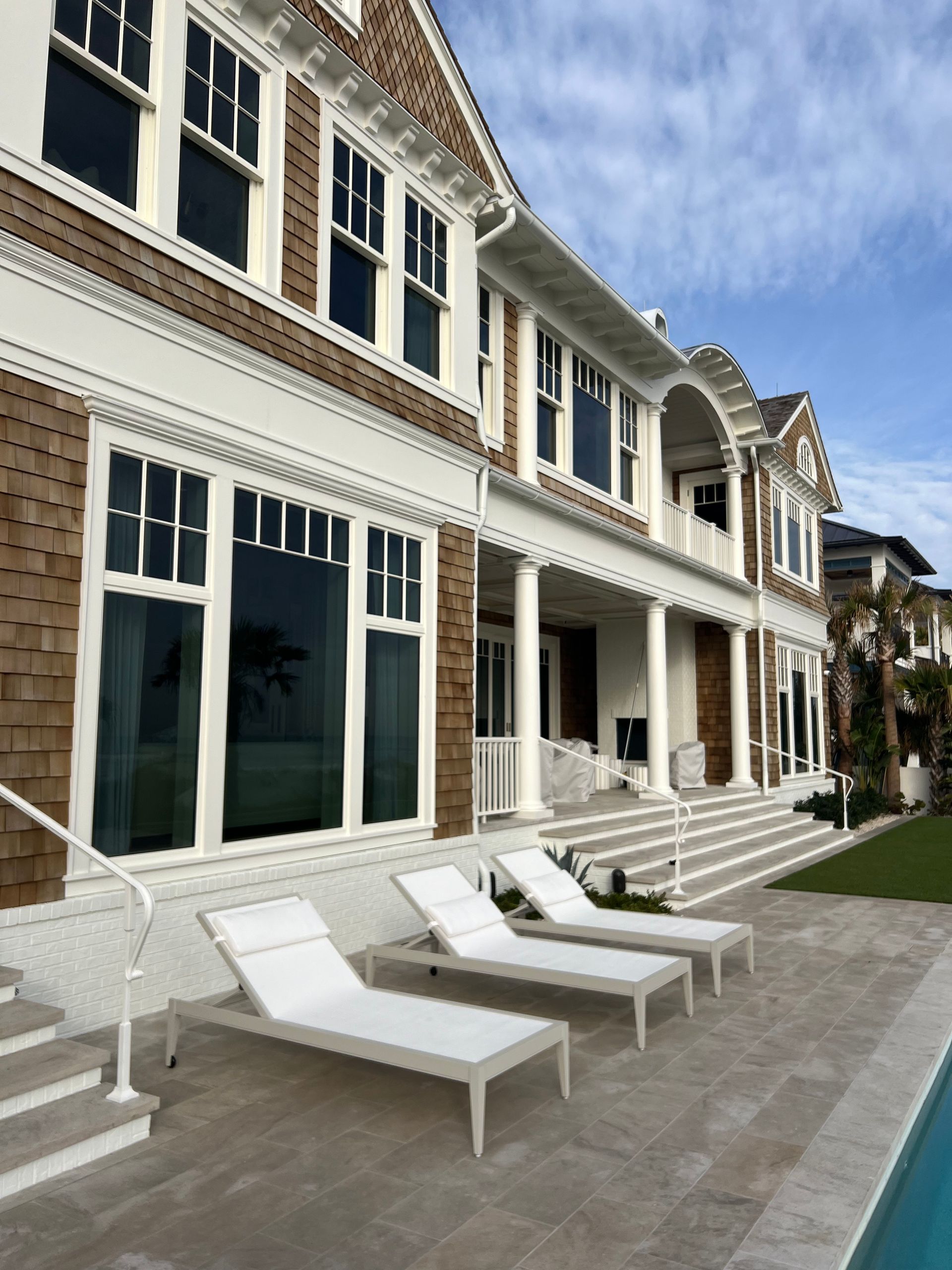 Luxurious multi-story house with pool, lounge chairs, and steps; neutral colors and blue sky.