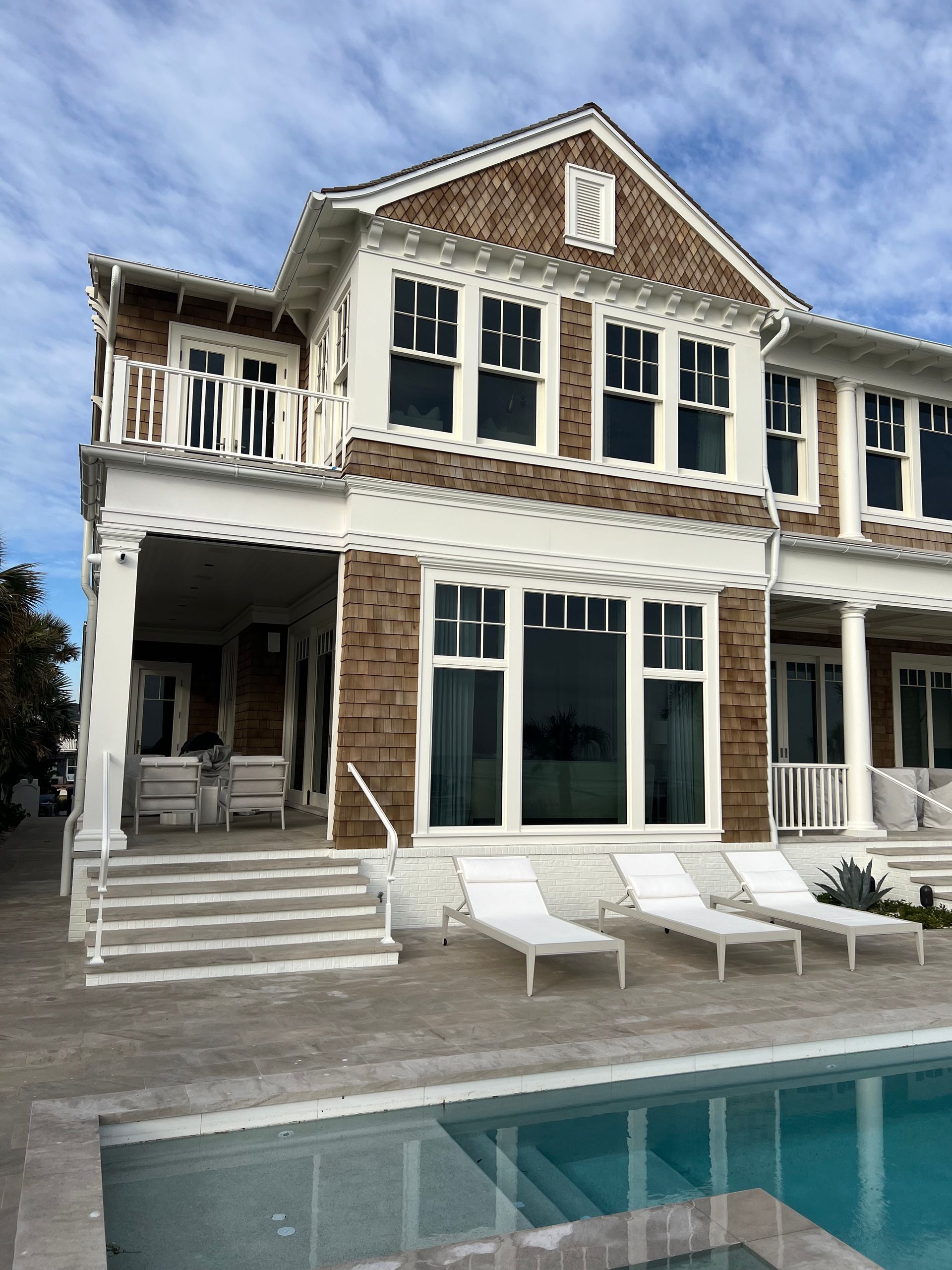 Two-story house with brick facade, balcony, and pool; chairs on patio.