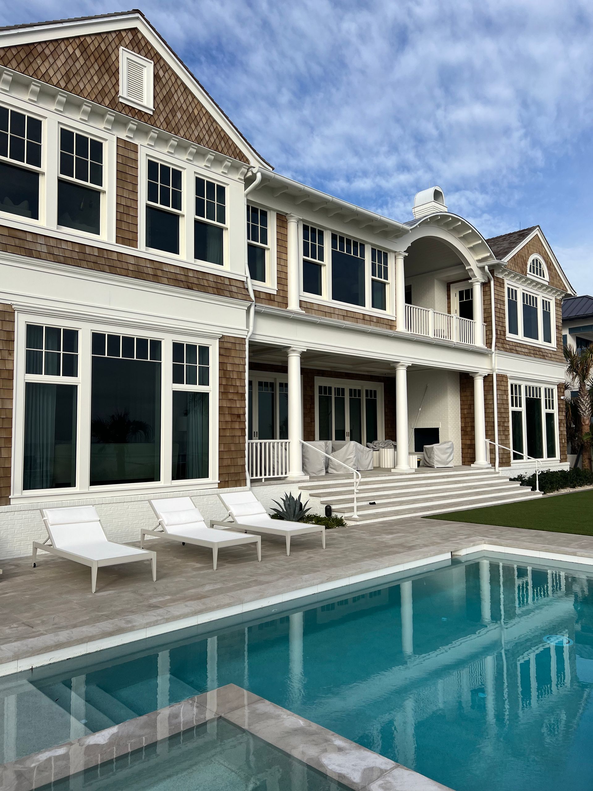 Luxury house with pool, featuring brown wood shingles, white trim, and blue water.
