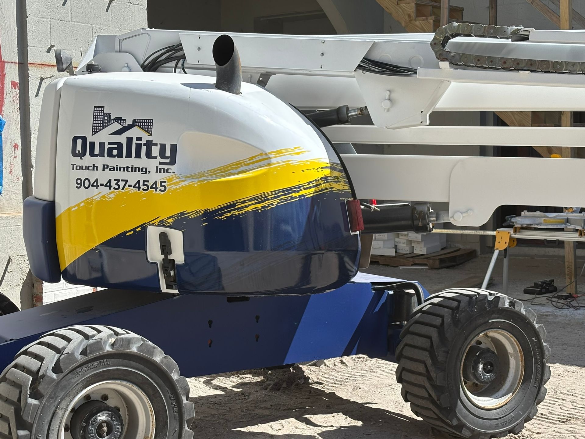 Blue and yellow Quality lift truck with black tires at a construction site.