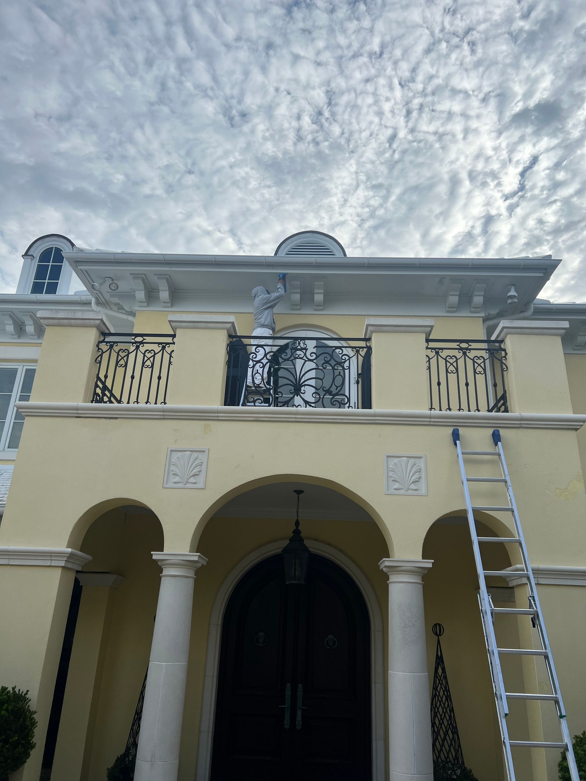 Yellow house with balcony and black wrought iron railing, a ladder leans against the building.